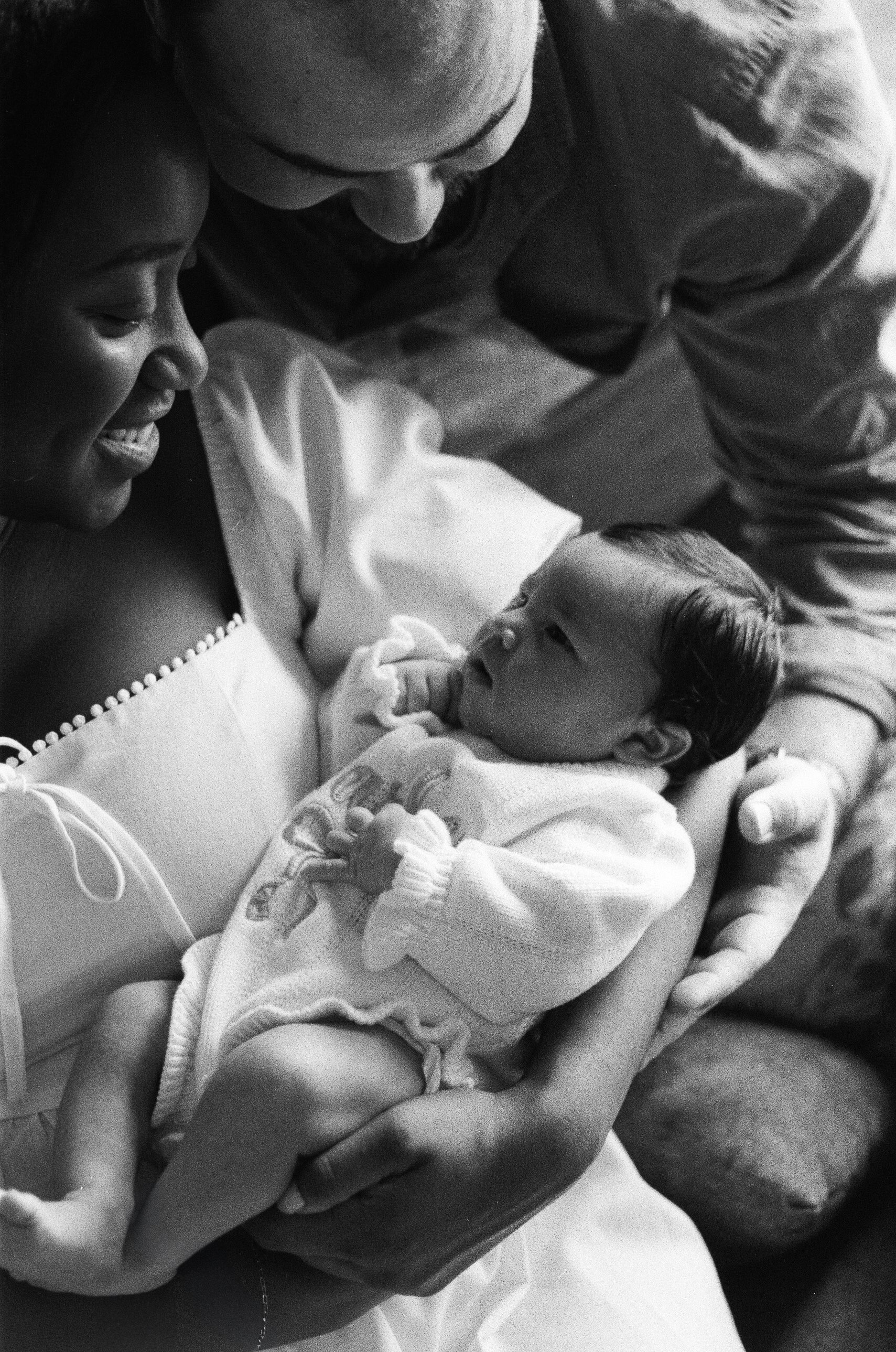 A woman holding a newborn baby while the man leans over and looks at the baby. The woman is smiling and the baby appears to be looking at her, in the Houston Ruby Postnatal. 