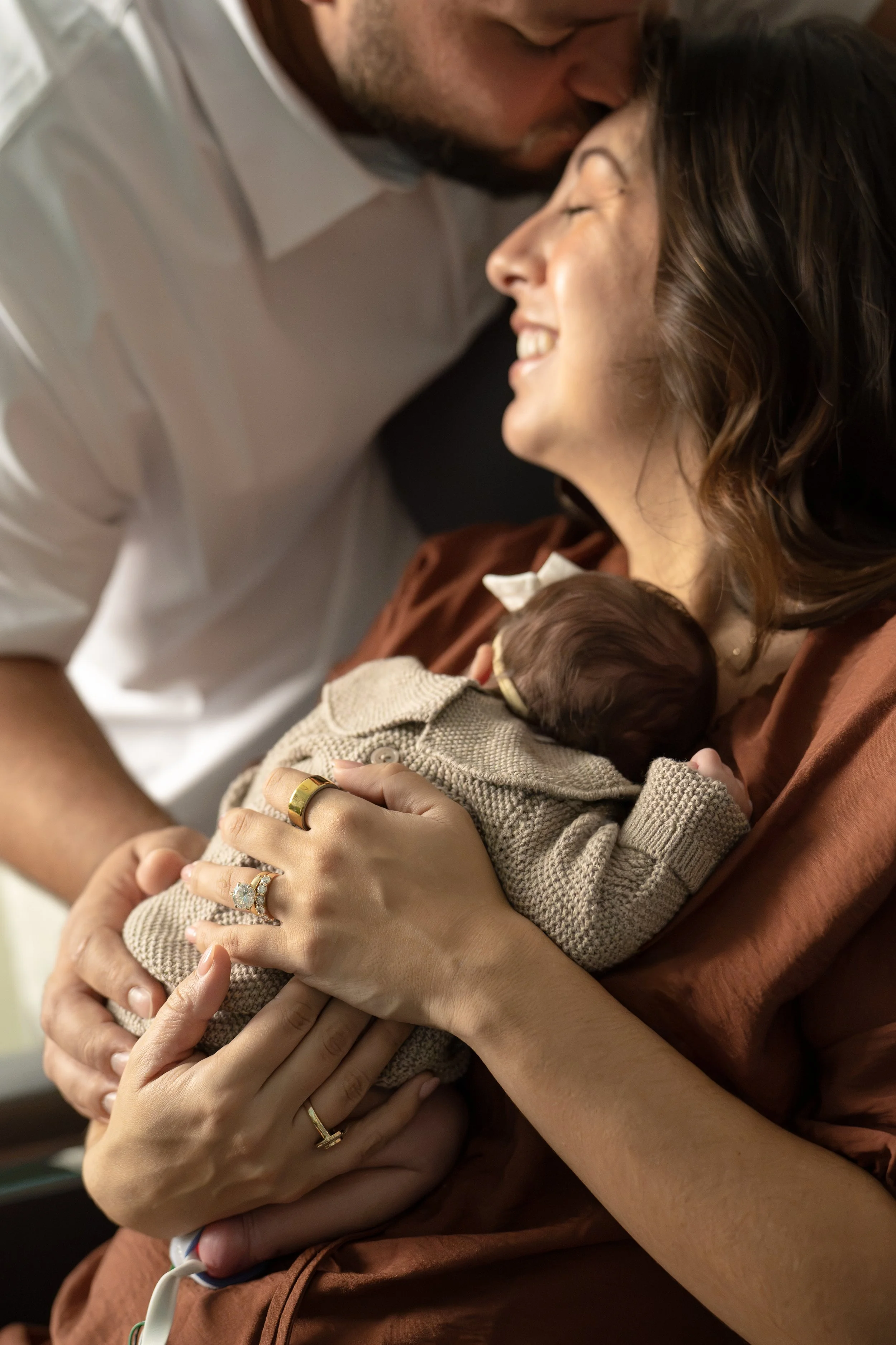 A woman holding a newborn baby close with both hands, smiling and resting her head on the baby's head at Houston medical center.