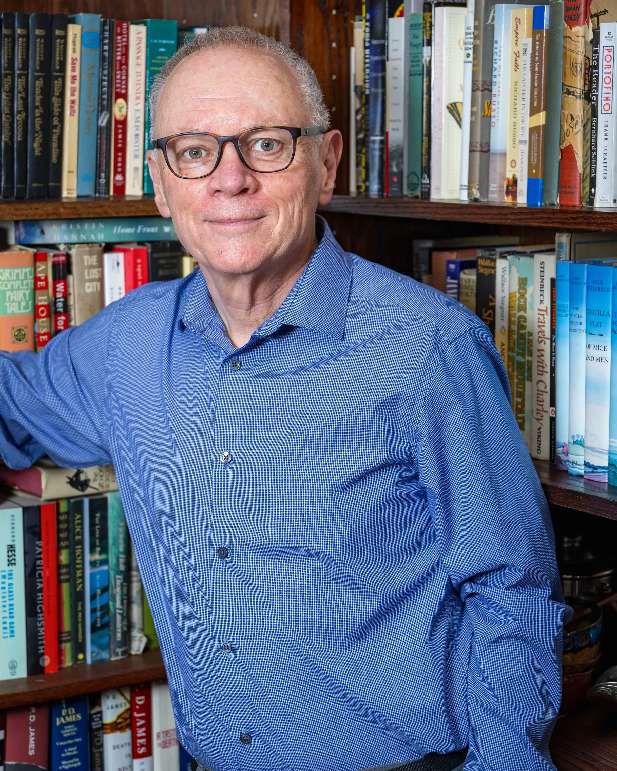 David Womack wearing a blue button-up shirt stands in front of bookshelves filled with colorful books.