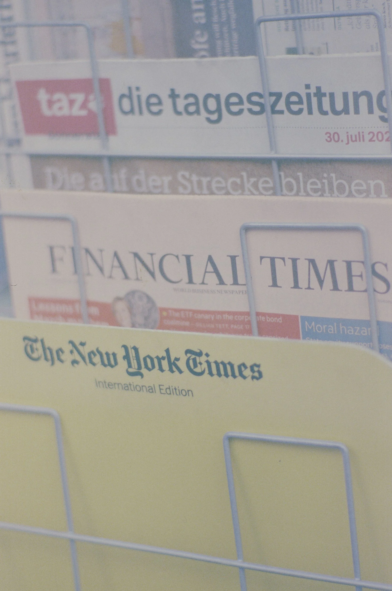 A display rack holding newspapers including 'die tageszeitung', 'Financial Times', and 'The New York Times'.