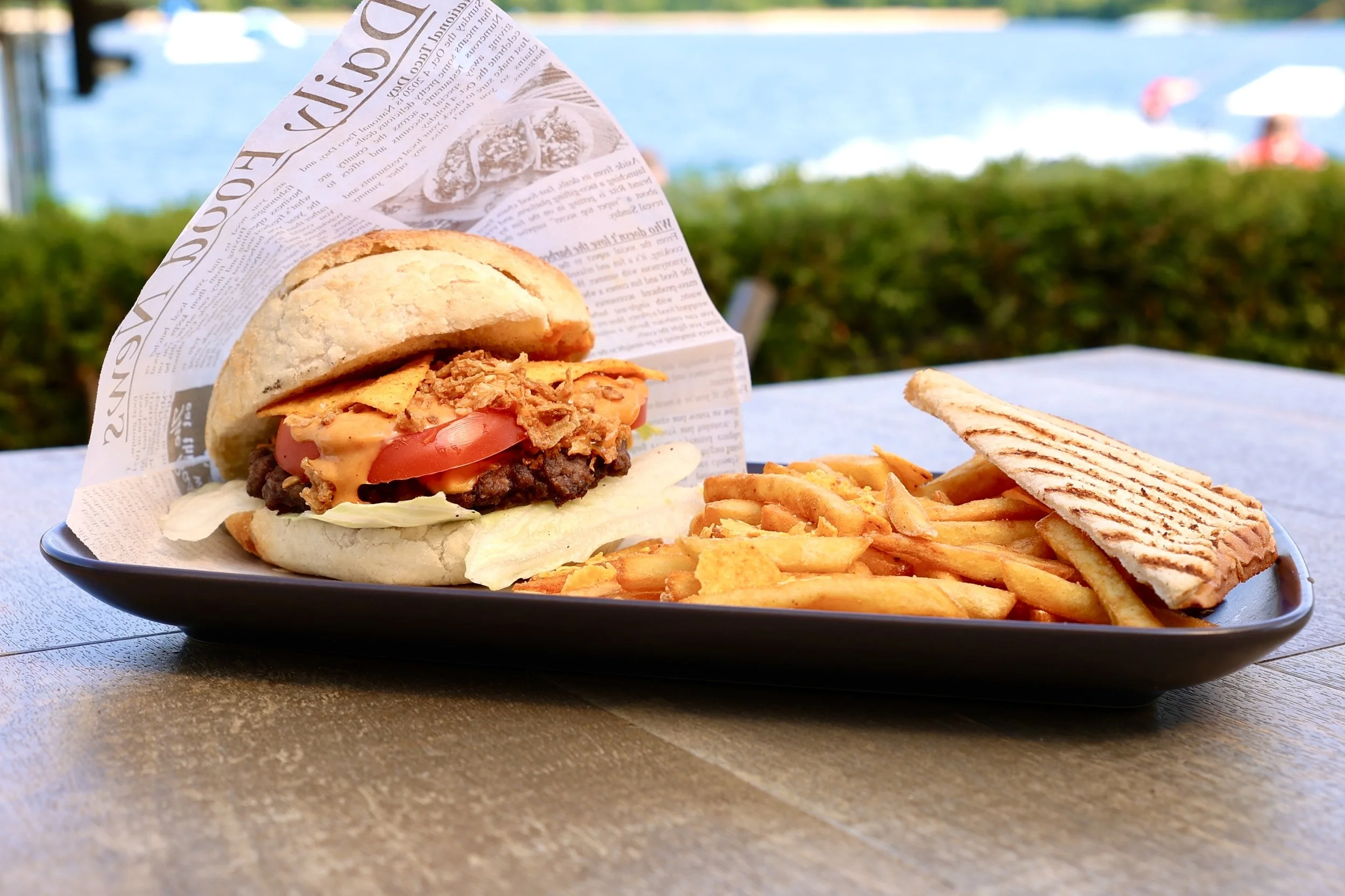 Ein Tray mit einem Burger, Pommes und Toast vor einem See im Freien.
