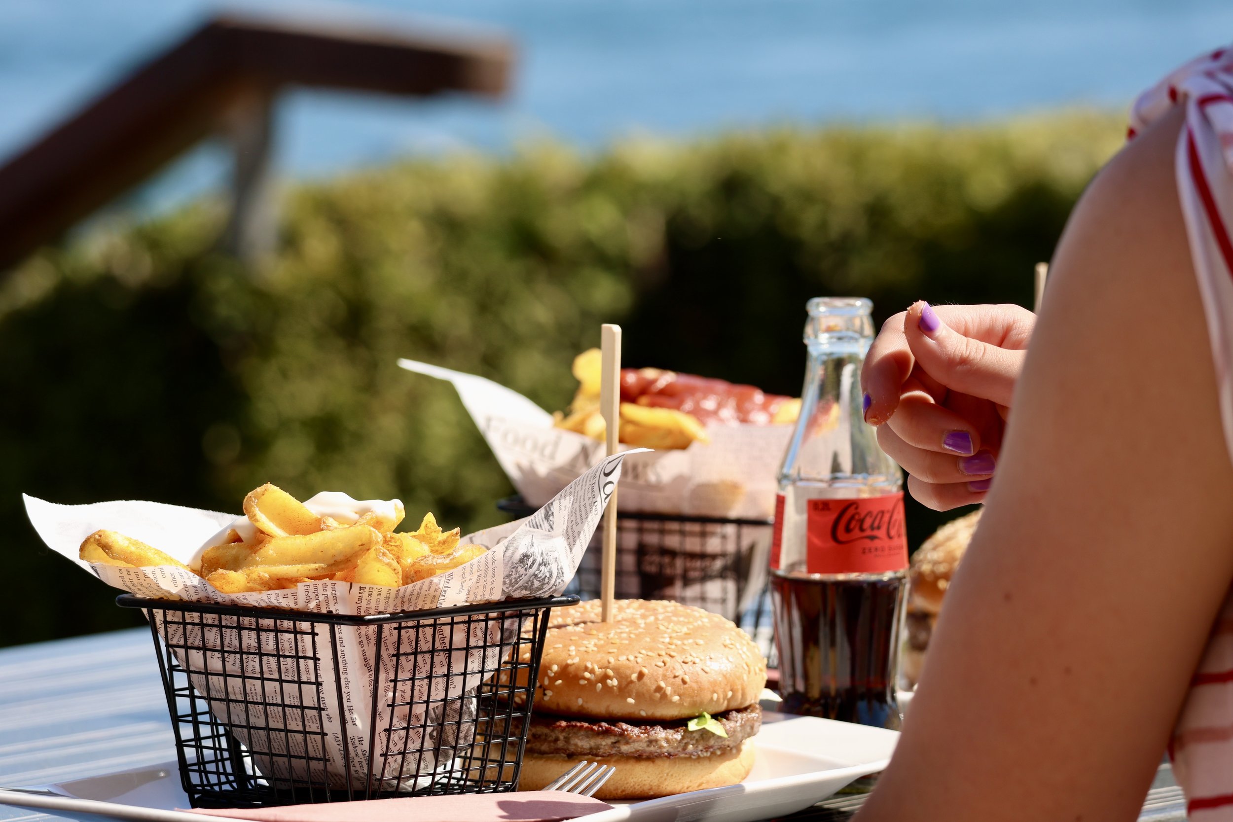 Fastfood-Mahlzeit mit Pommes, Hamburger, Cola-Flasche, und einem weiteren Burger im Freien an einem Tisch