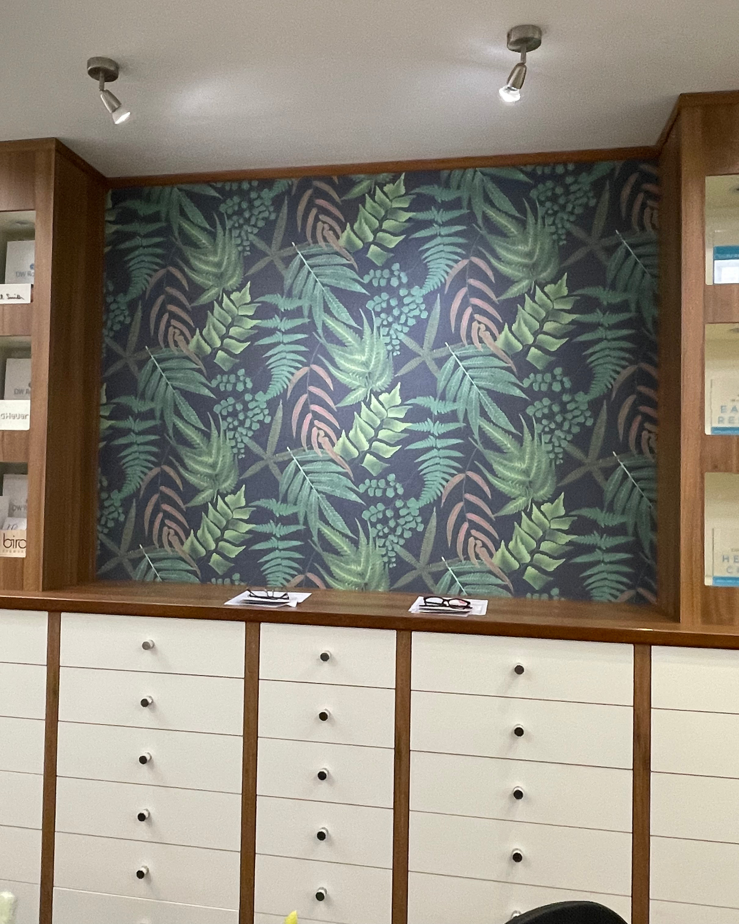 Interior with a wall featuring a tropical leaf pattern, flanked by wooden shelves with books, and a white cabinet with drawers in front.