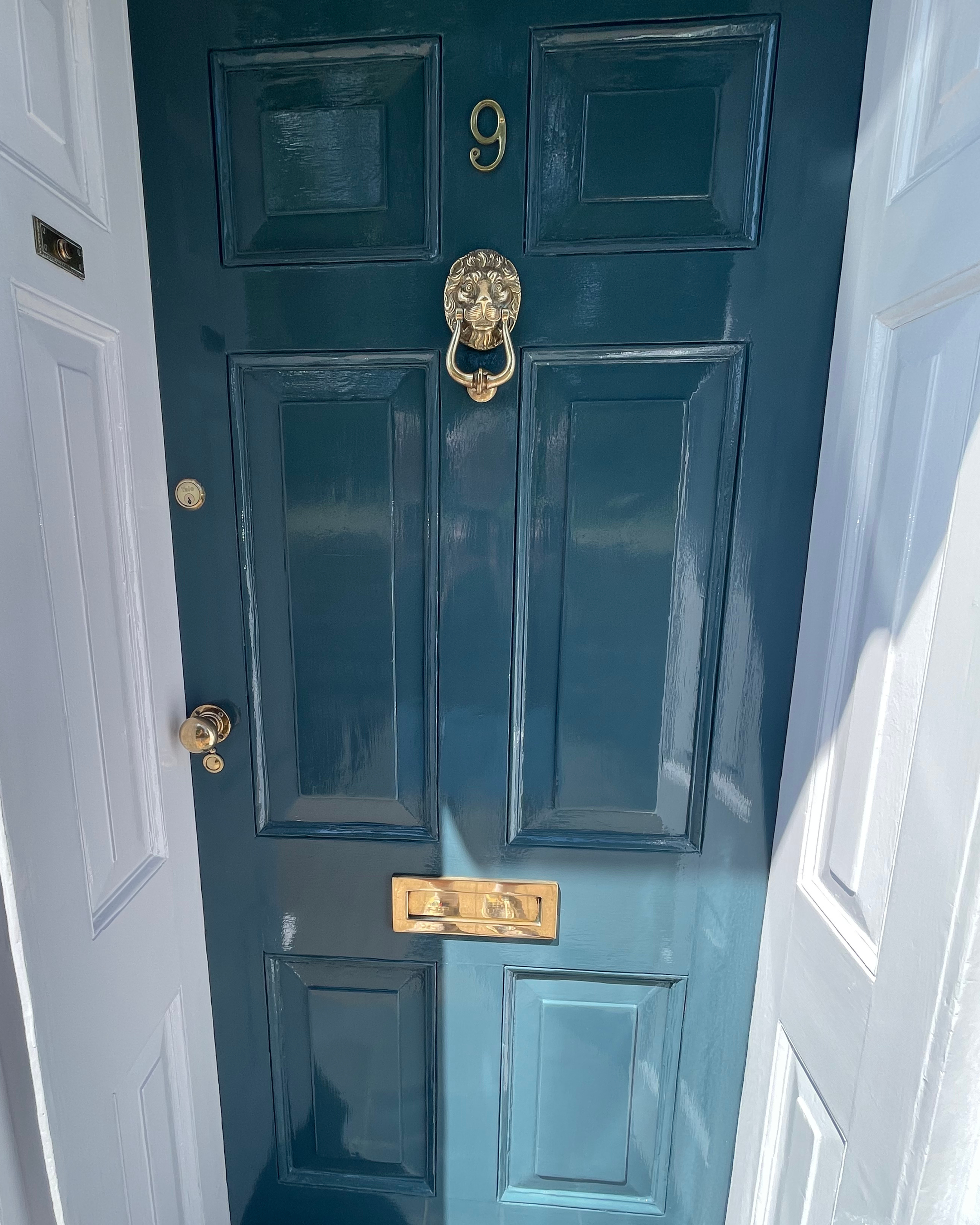 Blue front door with a lion's head door knocker, the number 9, and a gold mail slot, flanked by white side doors.