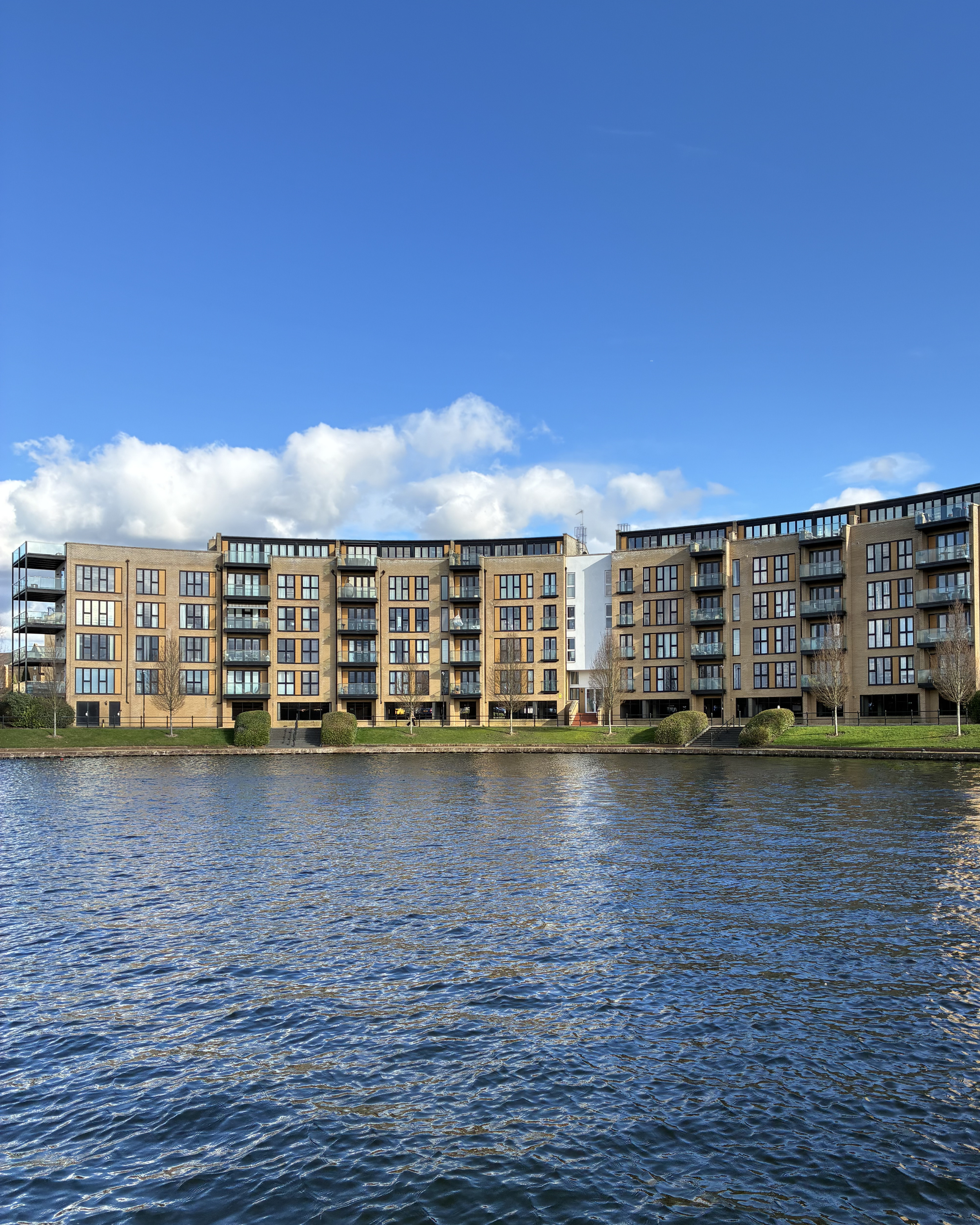 Modern apartment building along a waterway under a blue sky with clouds.