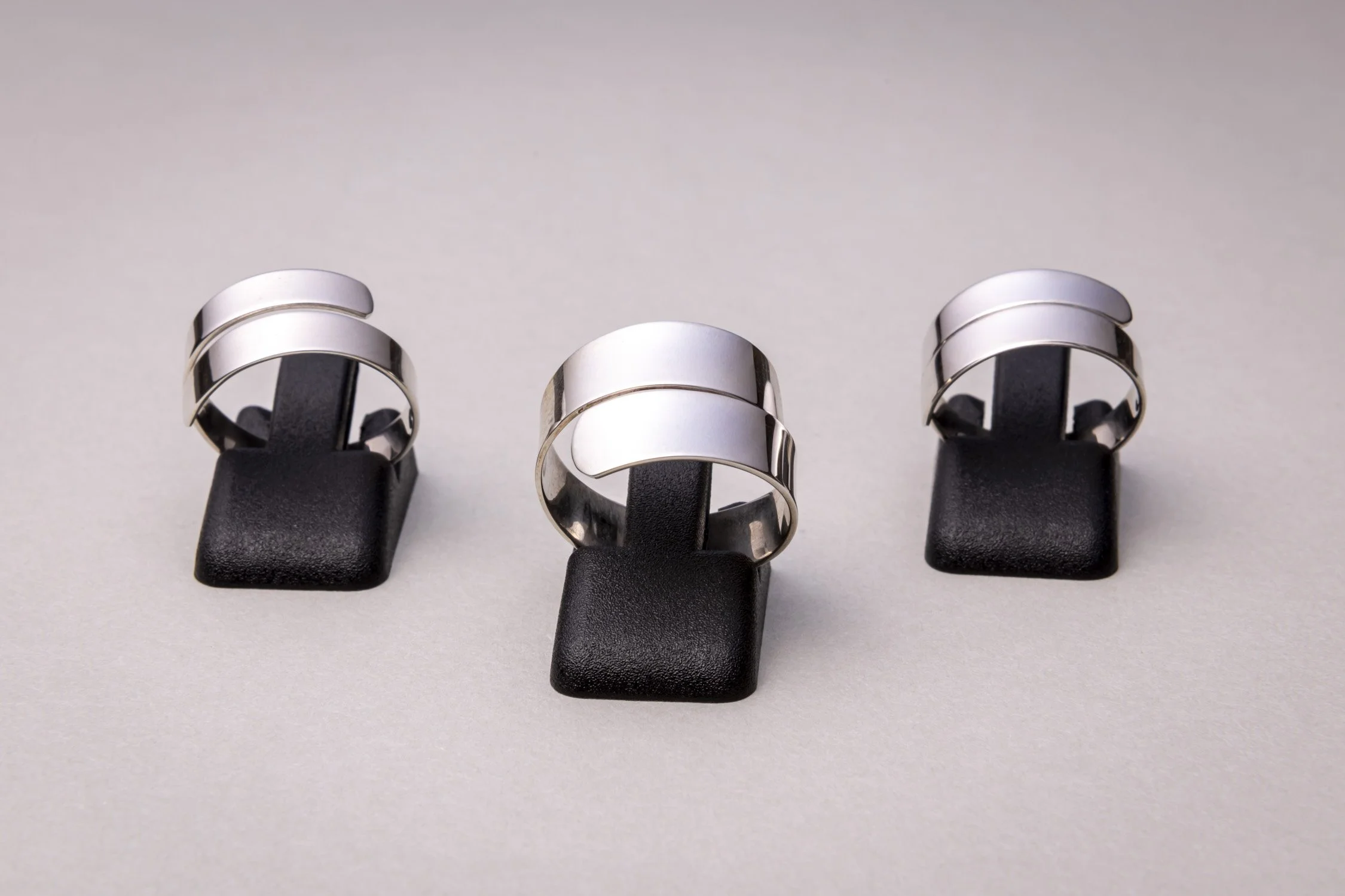 Three silver rings displayed on black ring holders against a plain beige background.