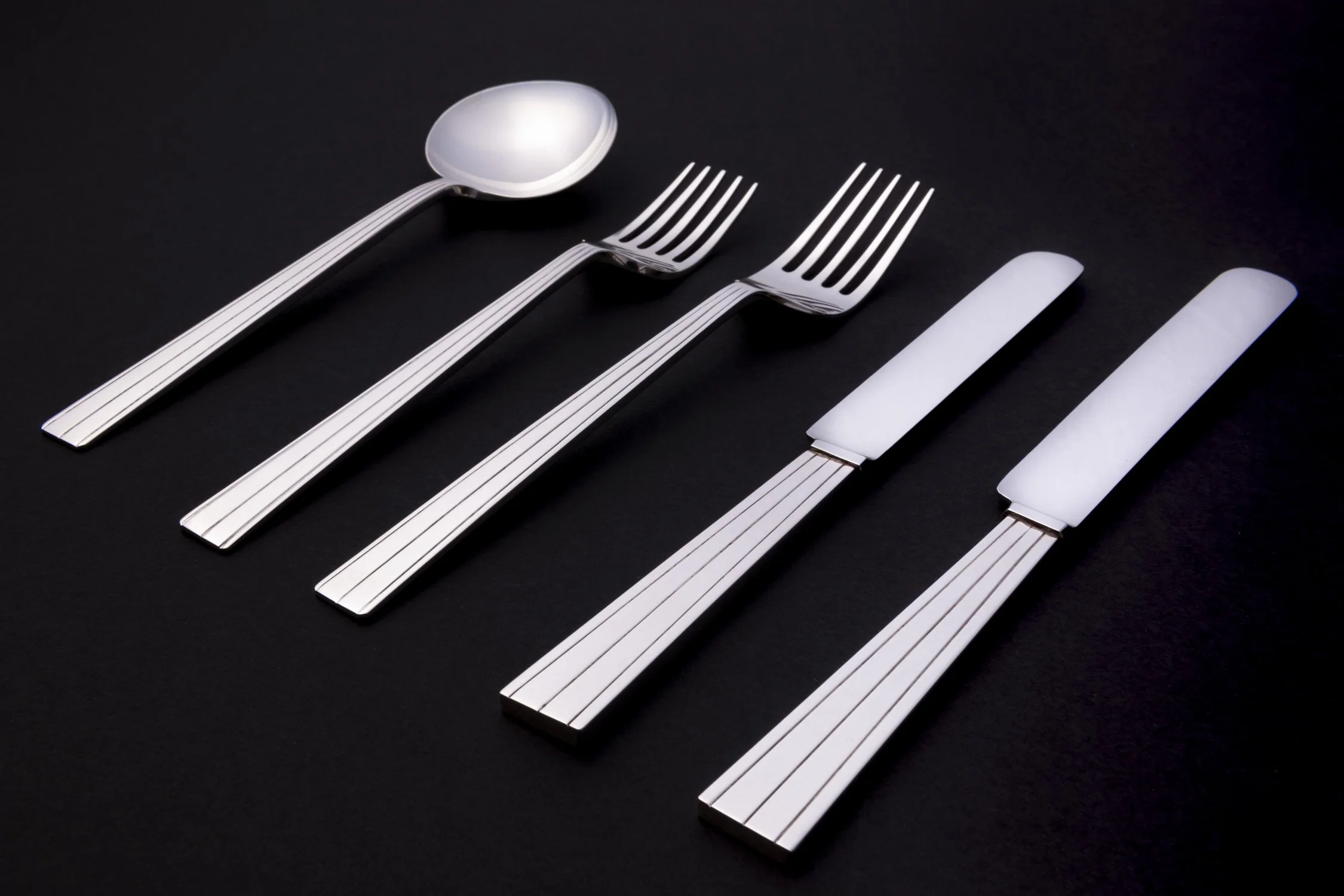 Set of silverware on black background including a spoon, two forks, and two knives.