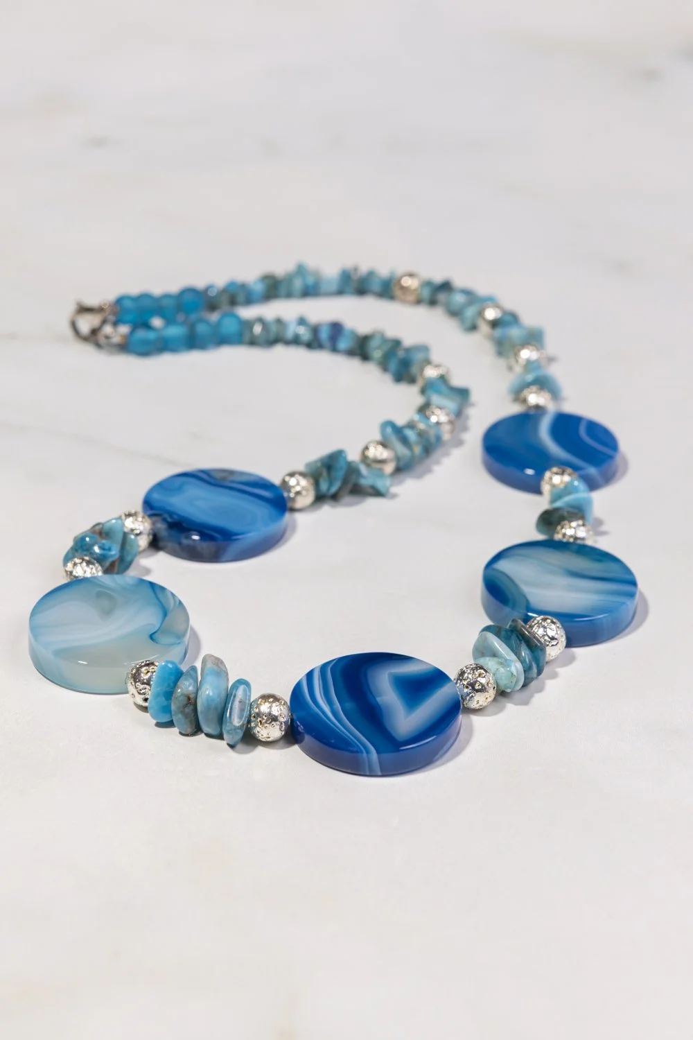 Blue and white beaded necklace with large marble-like round pendants and smaller silver and turquoise beads, laid on a white surface.
