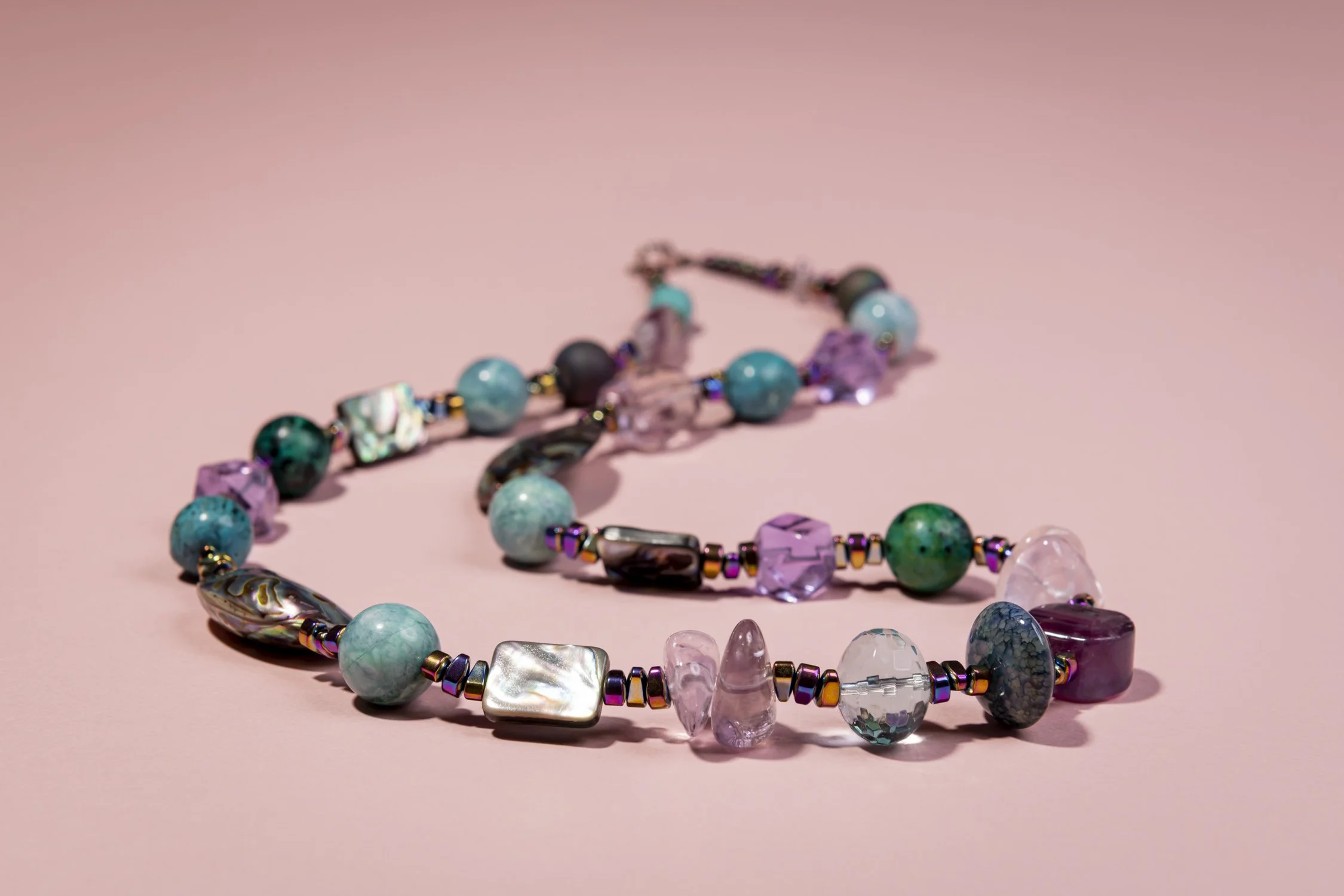 Colourful beaded necklace with various beads including crystals, and stones on a pink background.