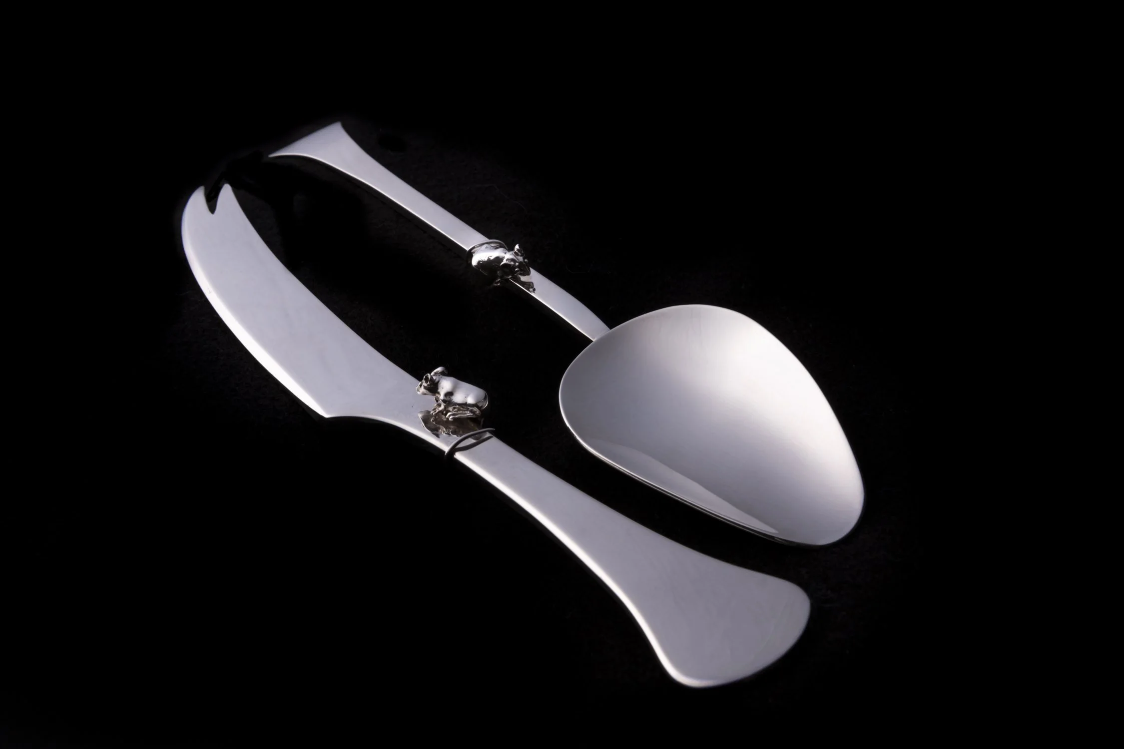 Elegant silver spoon and knife with decorative mouse-shaped motifs on the handles, placed on a black background.