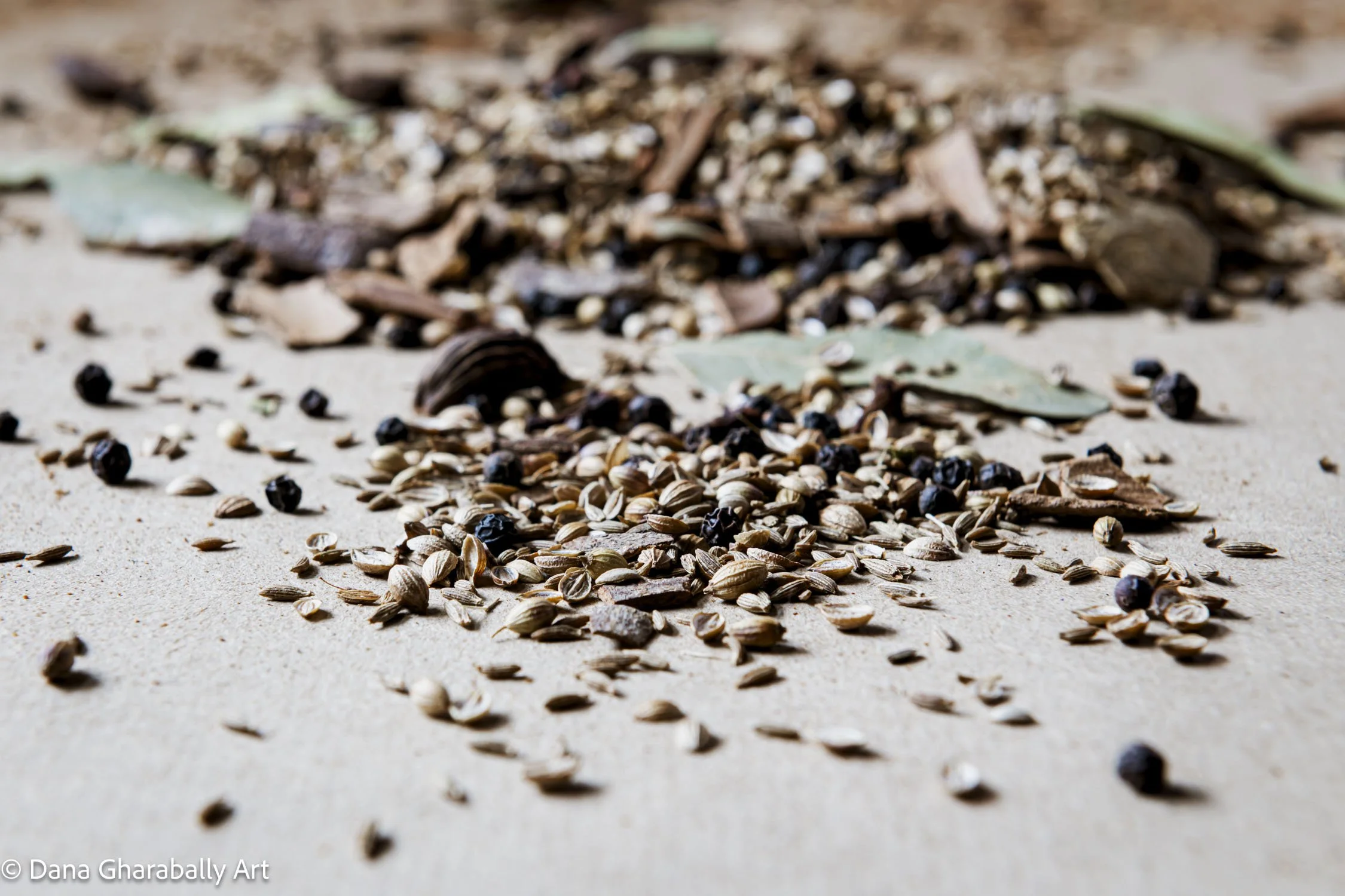 Close-up of scattered spices and dried bay leaves on a light beige background.
