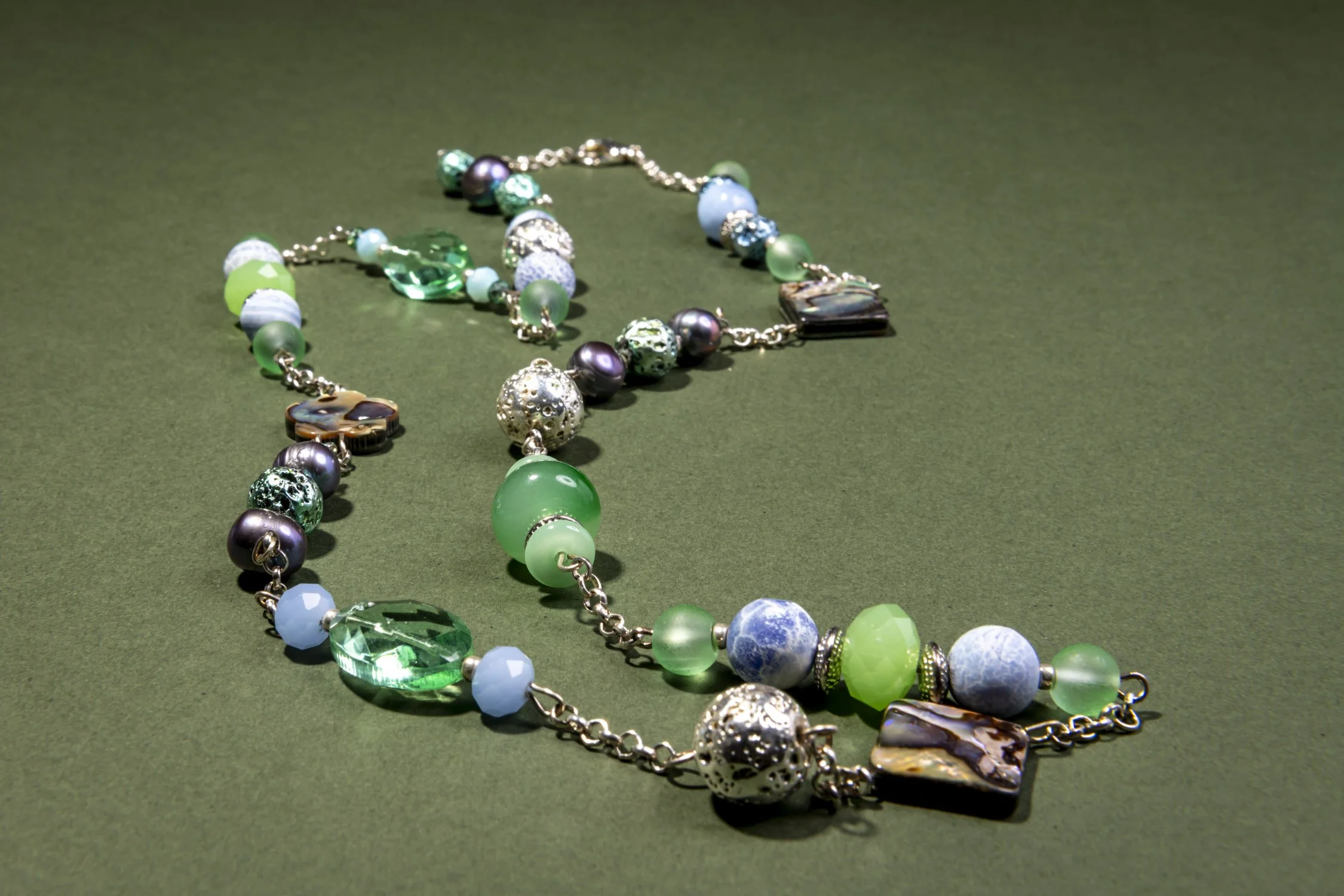 Colourful beaded necklace with green, blue, purple, and earth-toned beads on a green surface.