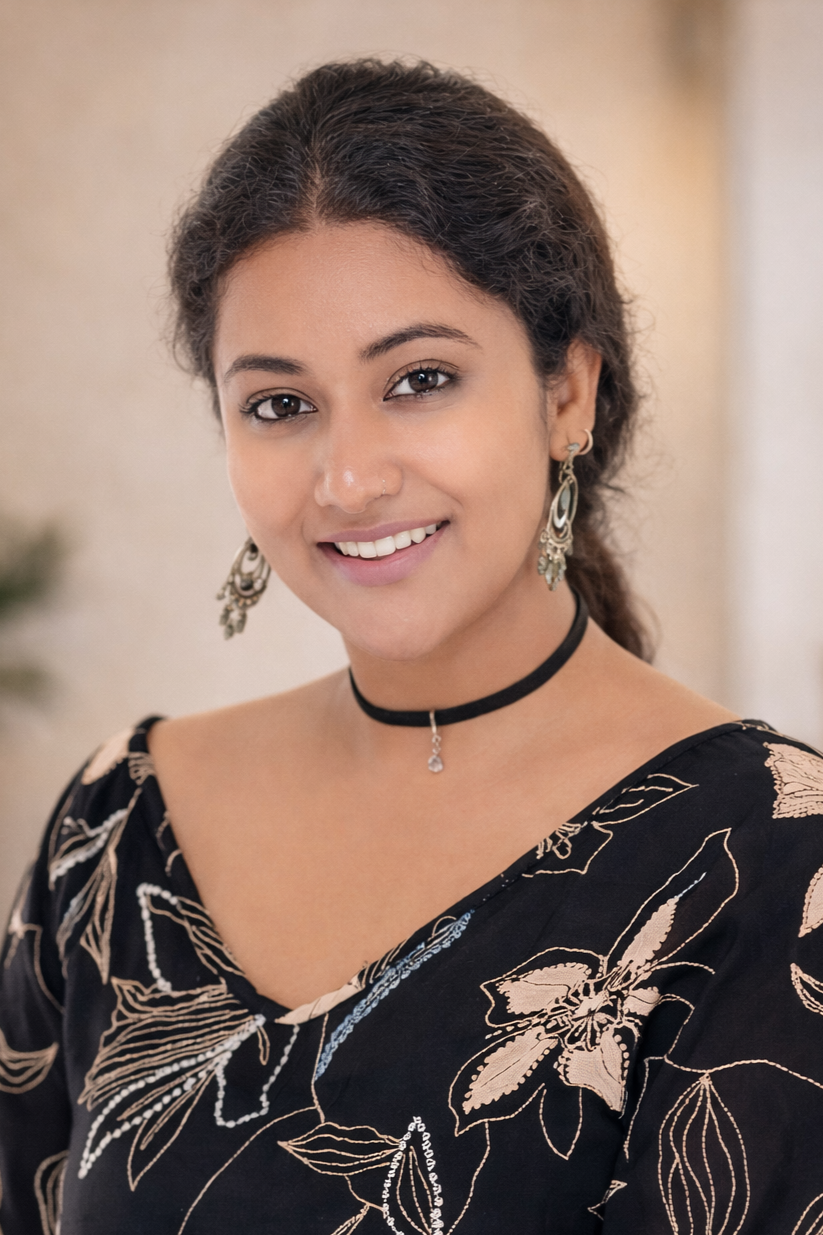 A young woman with curly brown hair, wearing a black floral dress, a black choker with a small pendant, and dangling earrings, smiling at the camera.