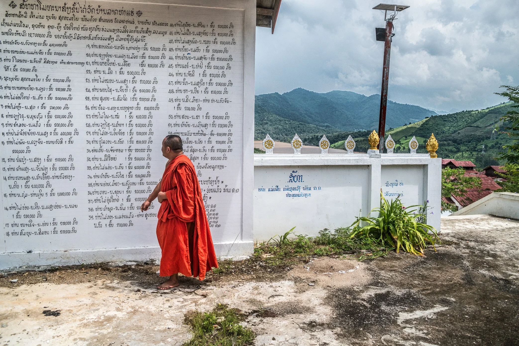 A monk stands beside the wall of a relocated village temple above the Nam Ou River, where the names of local donors are written in Lao script.

The original temple, like many homes along the river, was affected by the construction of the first Nam Ou