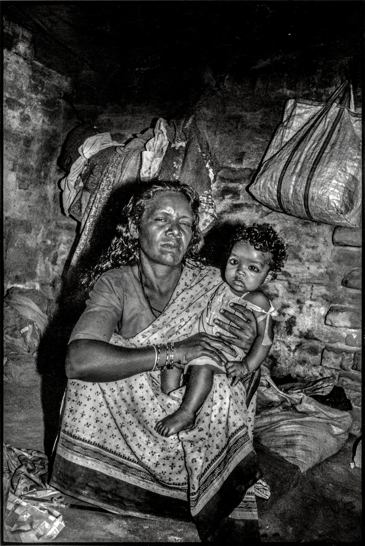 Patna, Bihar, India, April 2003 - Laxshmi, a brick kiln worker, holds her youngest daughter inside their living quarters near the kiln. For many girls born into this labor cycle, childhood offers little distance from the work that shaped their parent