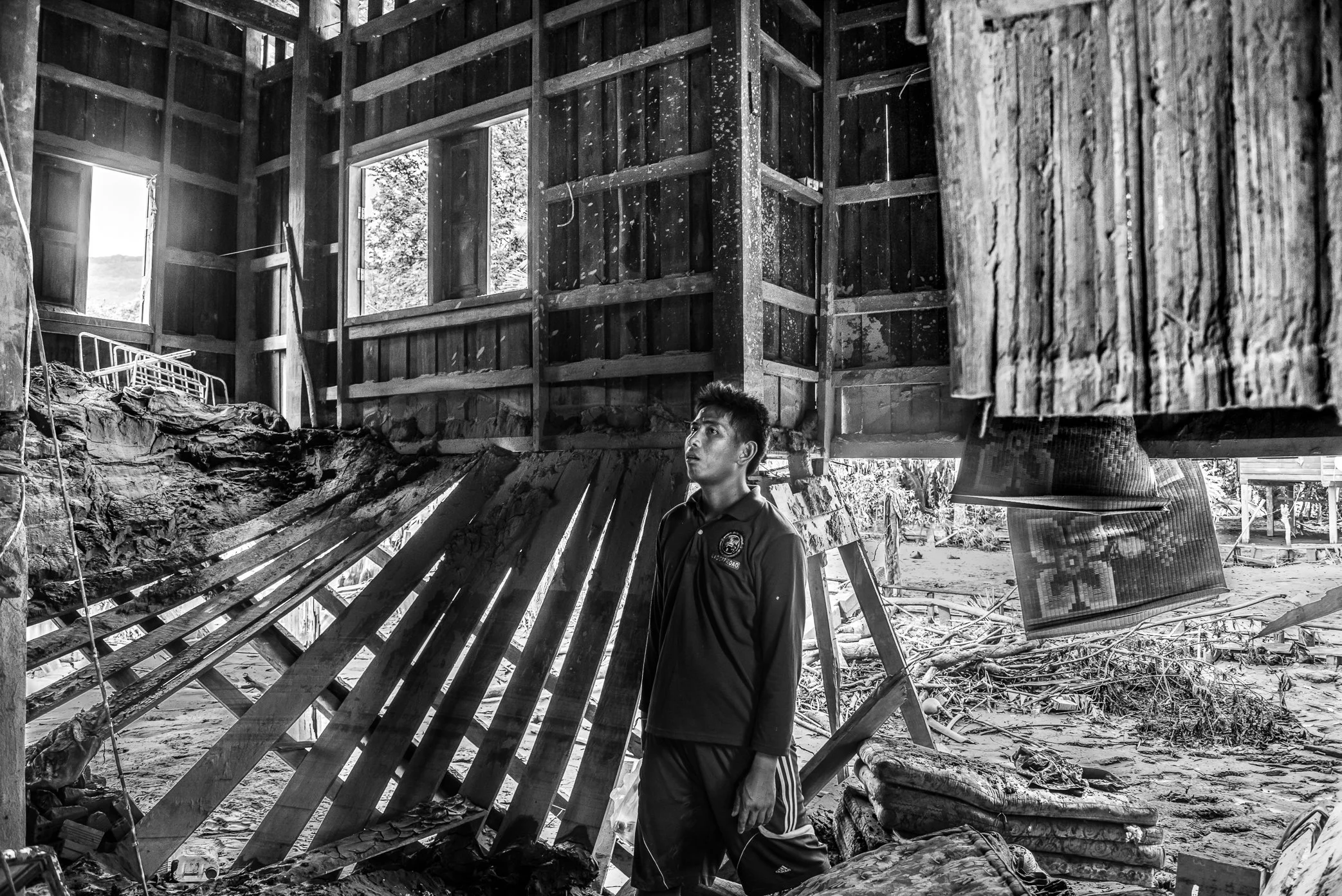 Hin Lat Village, Attapeu, Laos - A survivor stands inside what remains of his home after the Xe Pian dam collapse. Mud, debris, and floodwater have torn through the structure, leaving only fragments of the life that once filled it. In the silence aft