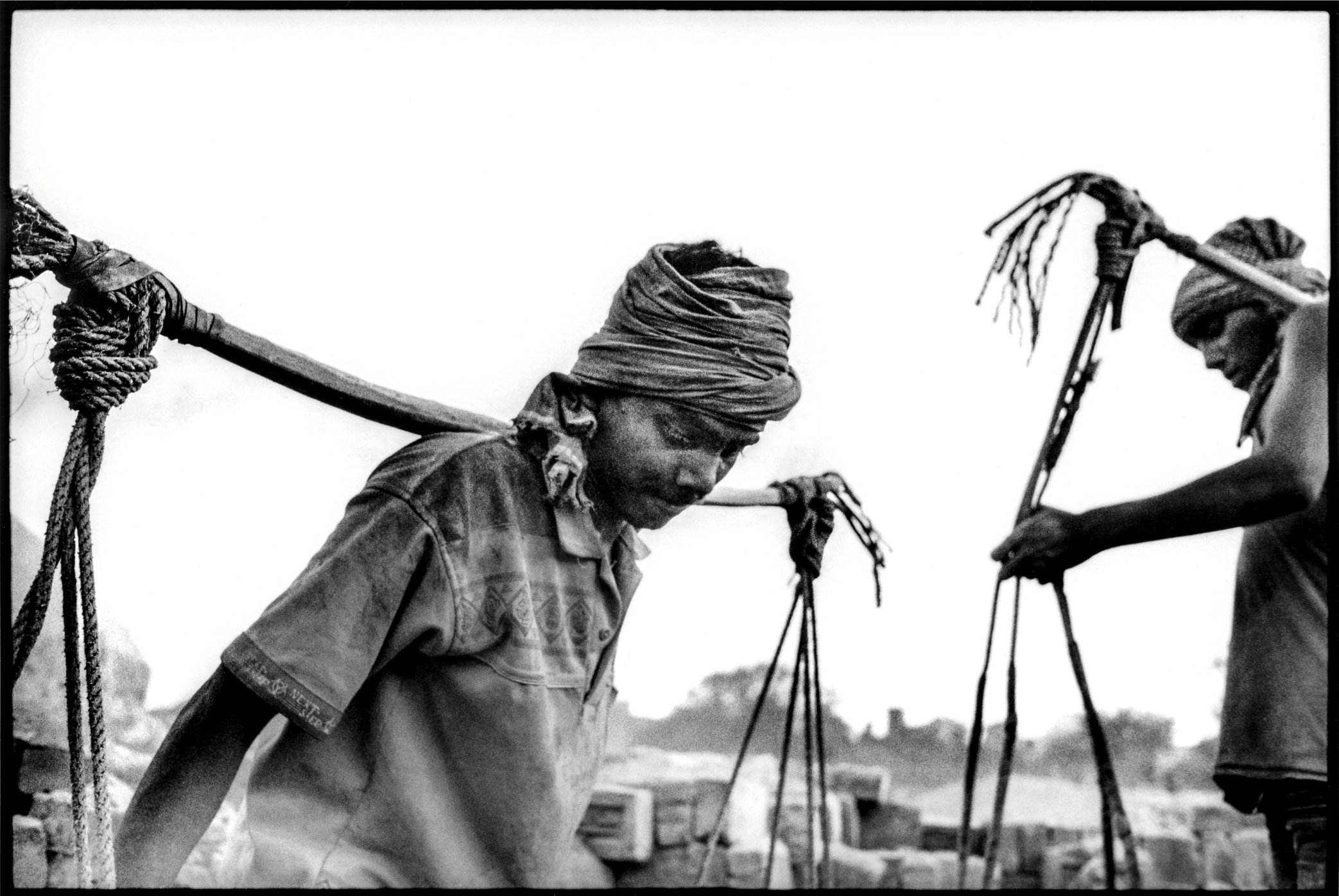Patna, Bihar, India, April 2003 - Men carry kiln-fired bricks in heavy double baskets slung from shoulder poles, while women move the same material balanced on their heads. At the kiln, the body itself becomes the main tool of labor.