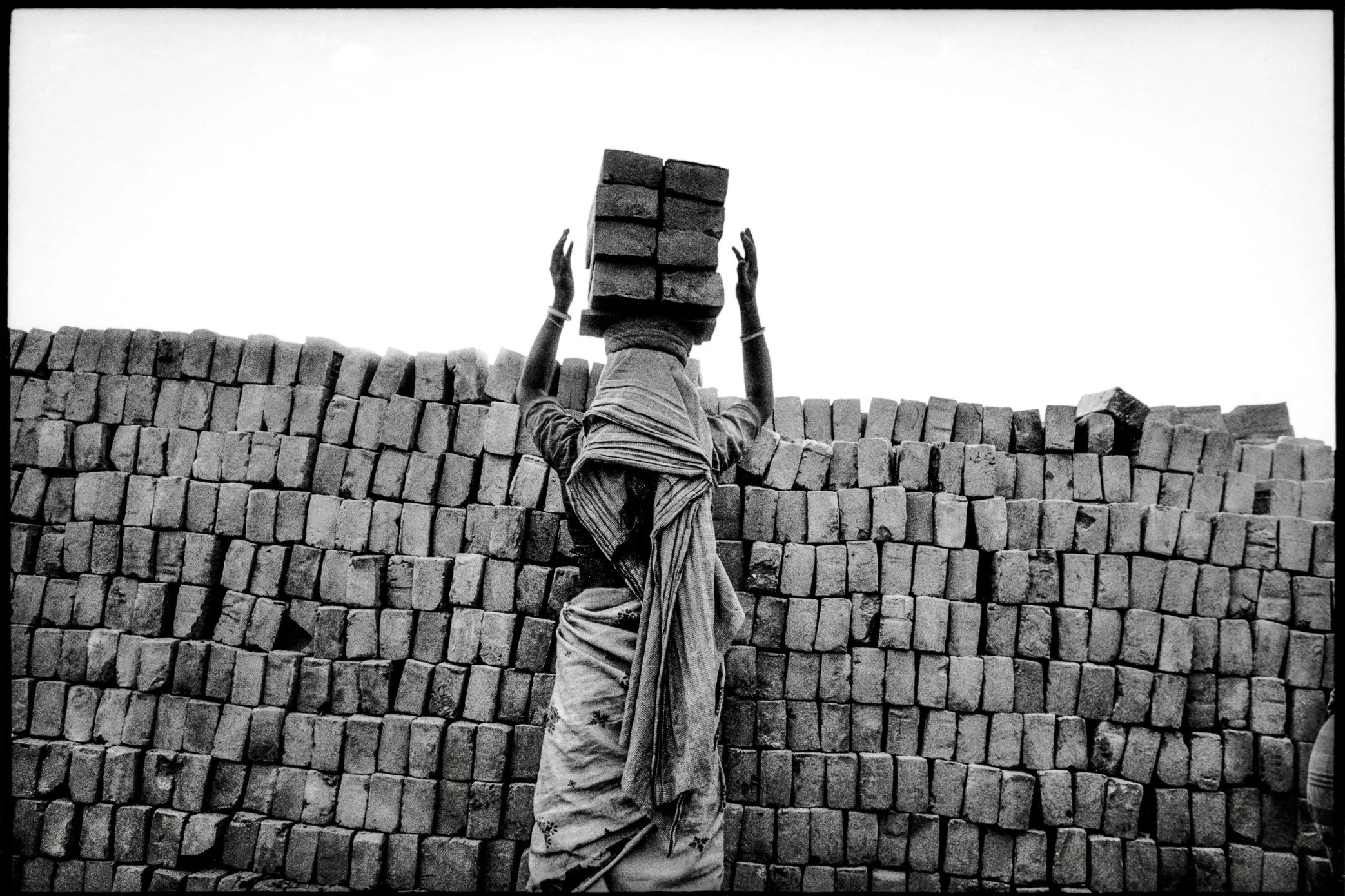 Patna, Bihar, India, April 2003 - A woman stacks freshly fired bricks at a kiln yard in Bihar. Men and women share the same punishing labor here, moving thousands of bricks by hand before they are transported and sold.