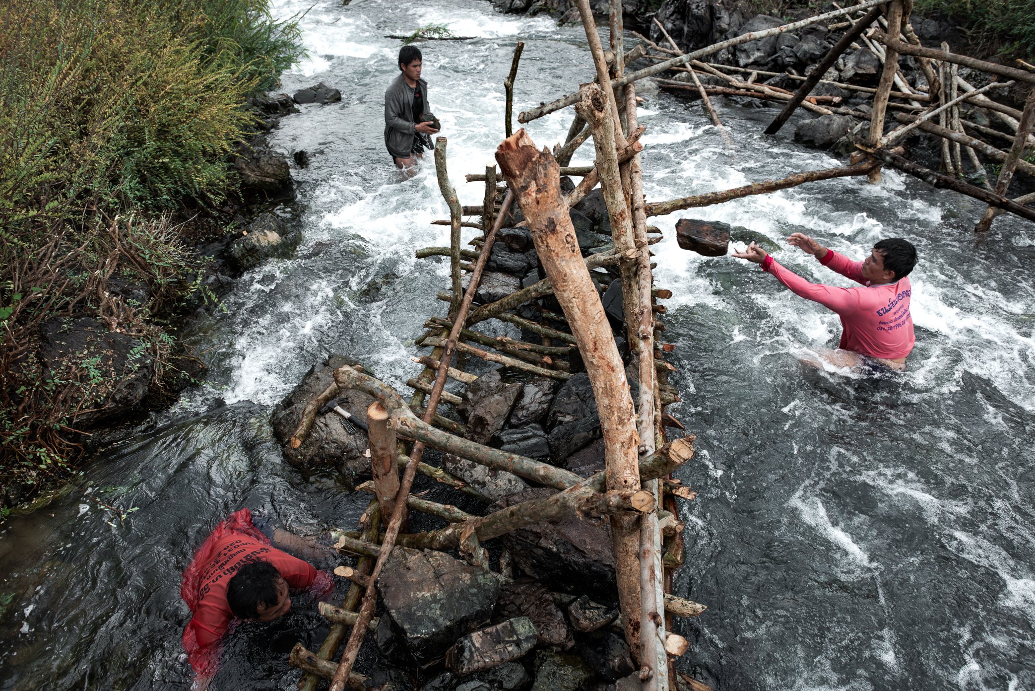 Fishermen work waist-deep in the current to build the stone foundation of a Li trap in Si Phan Don, southern Laos. Set in narrow channels where migratory fish are funneled by the force of the Mekong, these traditional traps must be anchored carefully