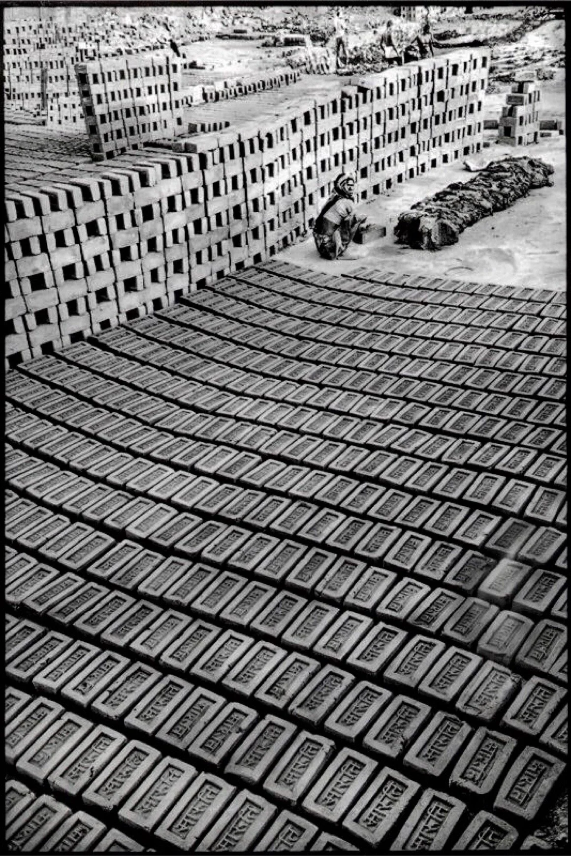 A construction site filled with stacks of bricks and a worker sitting nearby, with bricks arranged on the ground.