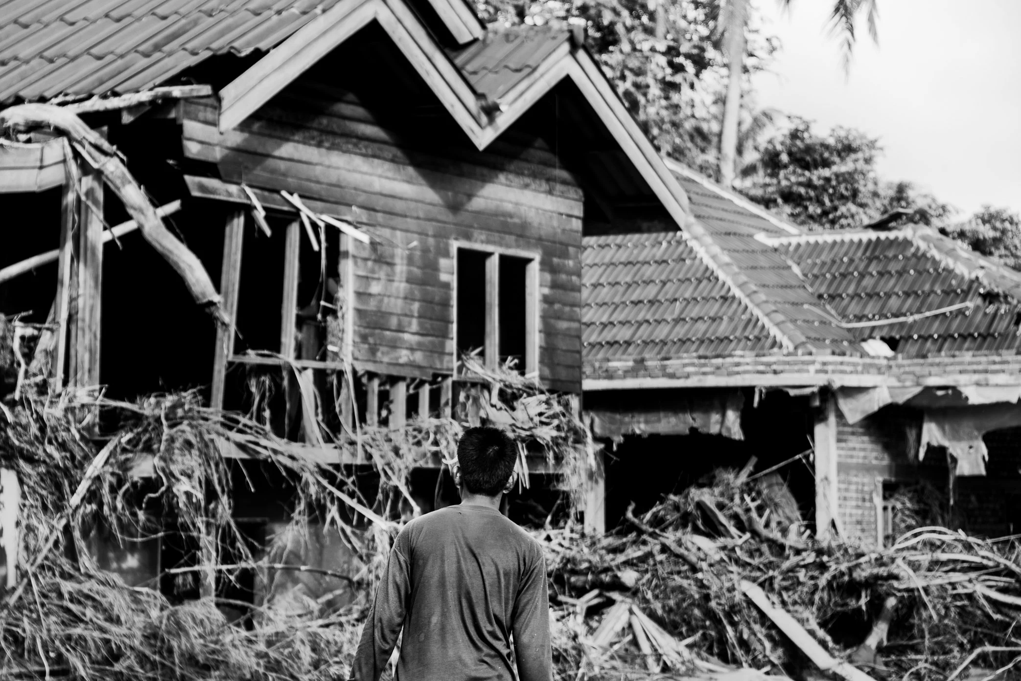 Hin Lat Village, Attapeu, Laos - A survivor stands before damaged homes in Hin Lat after the Xe Pian dam collapse. Scenes like this were visible throughout the village: houses torn open, walls broken, and debris left hanging from the structures that 