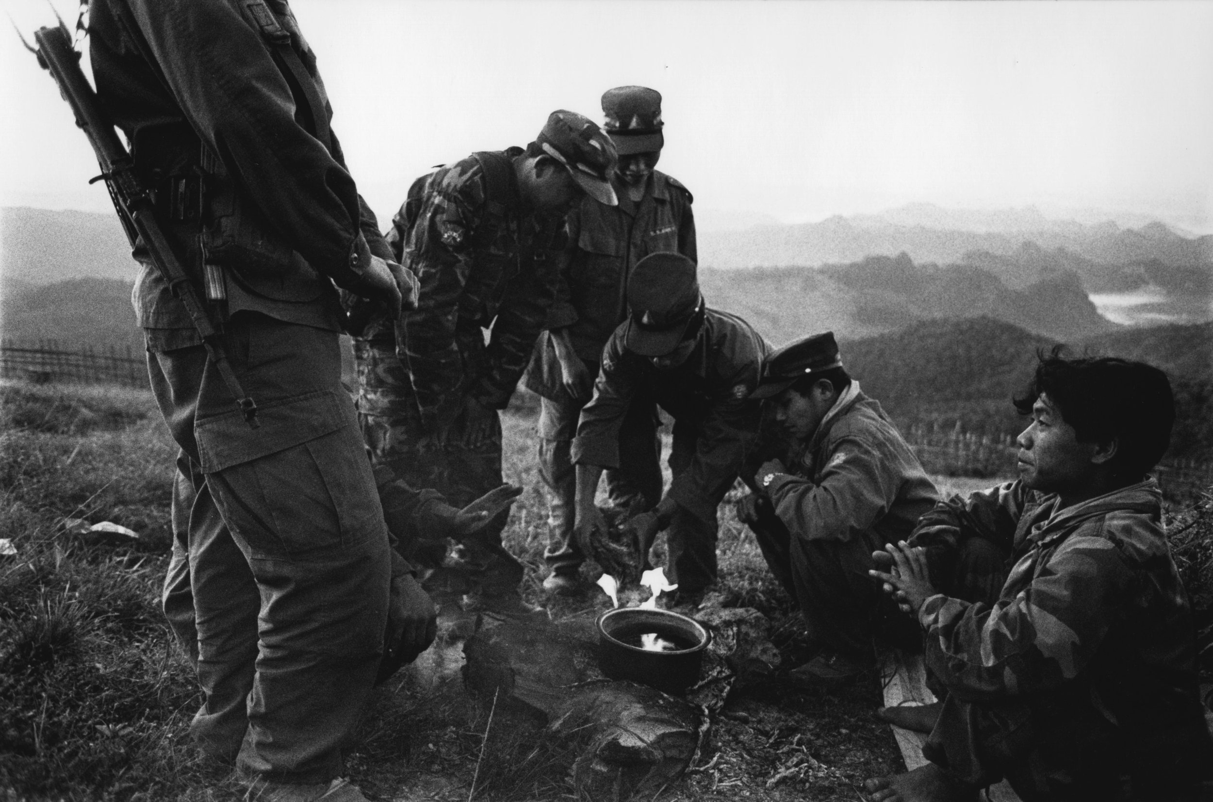 Group of soldiers performing a ritual or prayer around a small campfire on a hillside, in black and white.