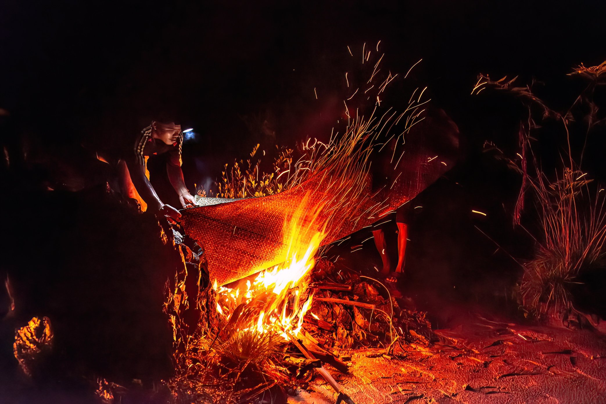 At a remote Li trap site in Si Phan Don, fishermen dry their sleeping mat over an open fire after a night storm. During the migration season, they live for days or weeks beside the traps, often in shelters made only from bamboo frames and tarpaulin, 