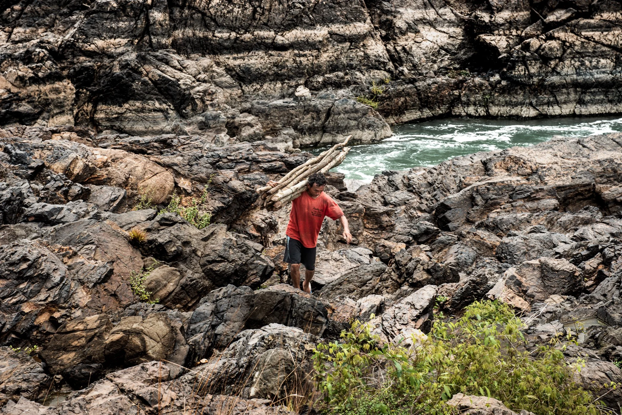 Carrying freshly cut poles across black volcanic rock, a fisherman brings material to a remote trap site where a new Li is taking shape. Before the fishing season begins, men must gather wood from nearby areas and haul it by hand through broken terra