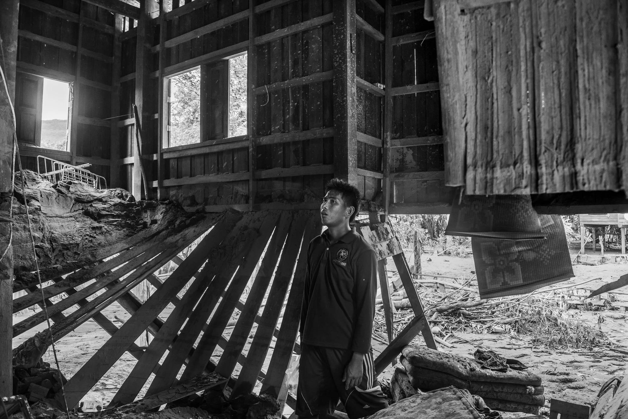 Hin Lat Village, Attapeu, Laos - A survivor stands inside what remains of his home after the Xe Pian dam collapse. Mud, debris, and floodwater have torn through the structure, leaving only fragments of the life that once filled it. In the silence aft