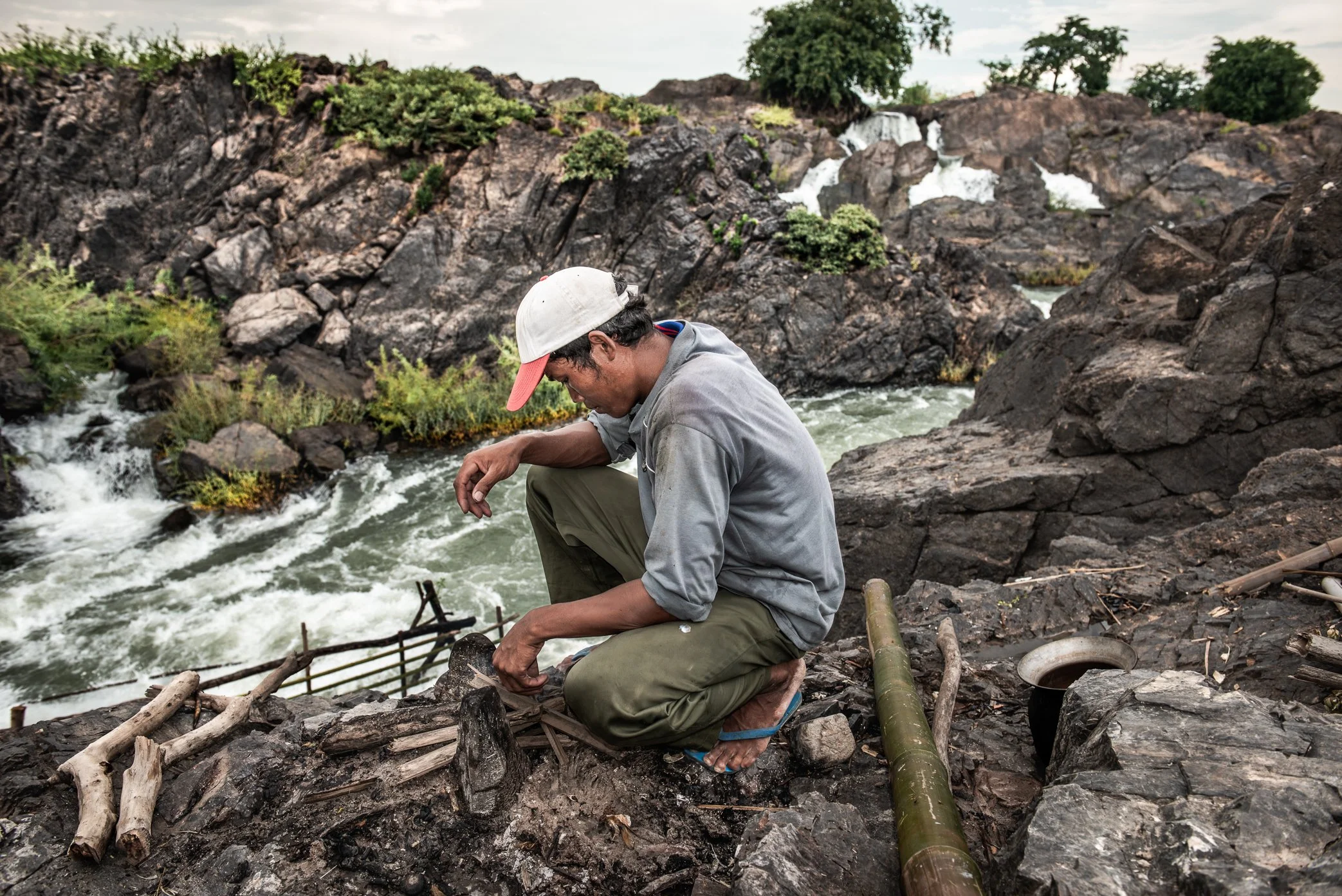 A fisherman pauses beside the remains of a damaged Li trap in Si Phan Don, where a night of hard rain and rising water has undone days of labor. Built from wood, bamboo, and stone, these traditional traps depend on a foundation strong enough to withs