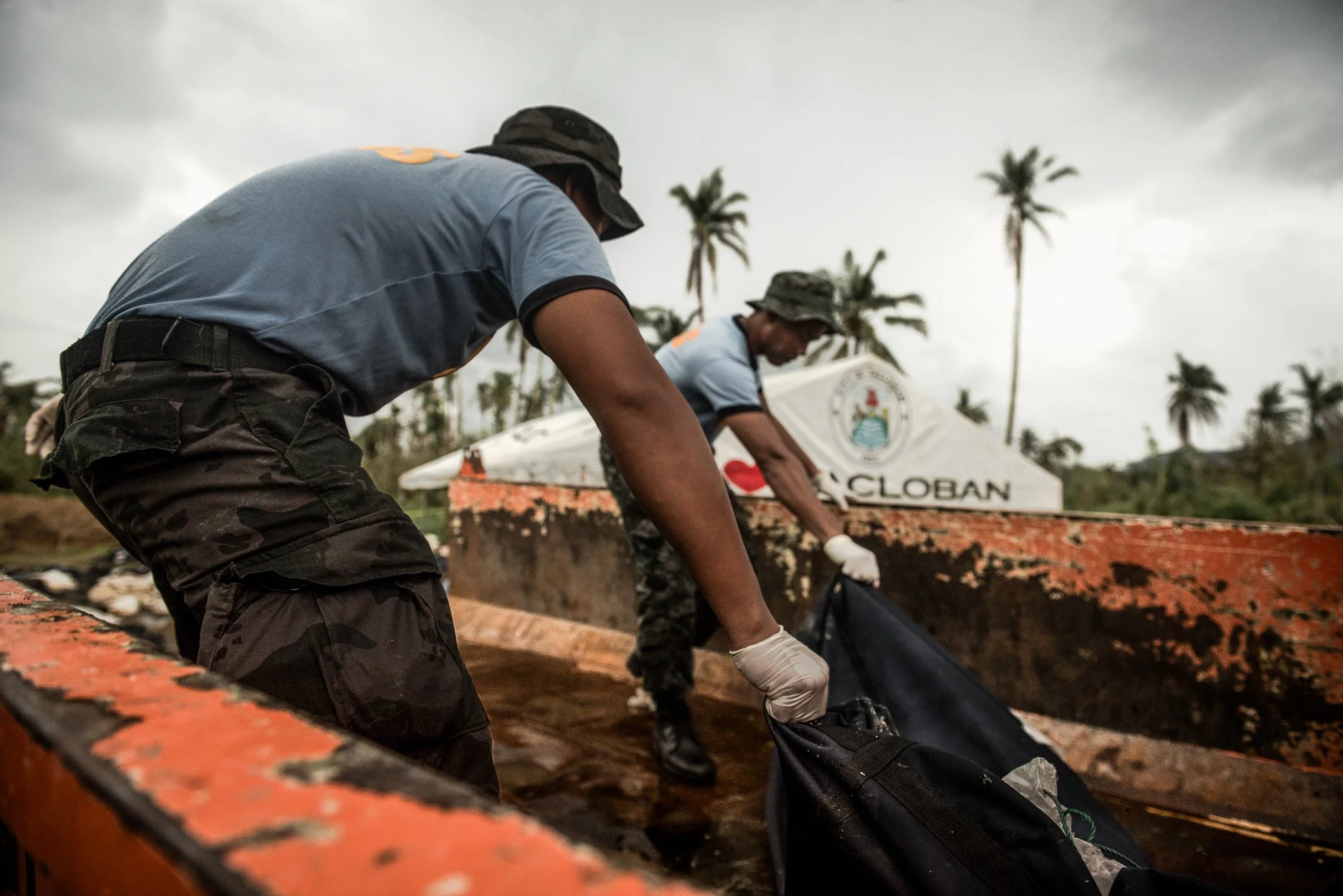 Philippines, 2013 - Three weeks after Typhoon Haiyan, members of a special police unit unload bodies recovered from the ruins. Each day, more victims were found and brought to burial sites like this one, where the scale of loss overwhelmed ordinary r
