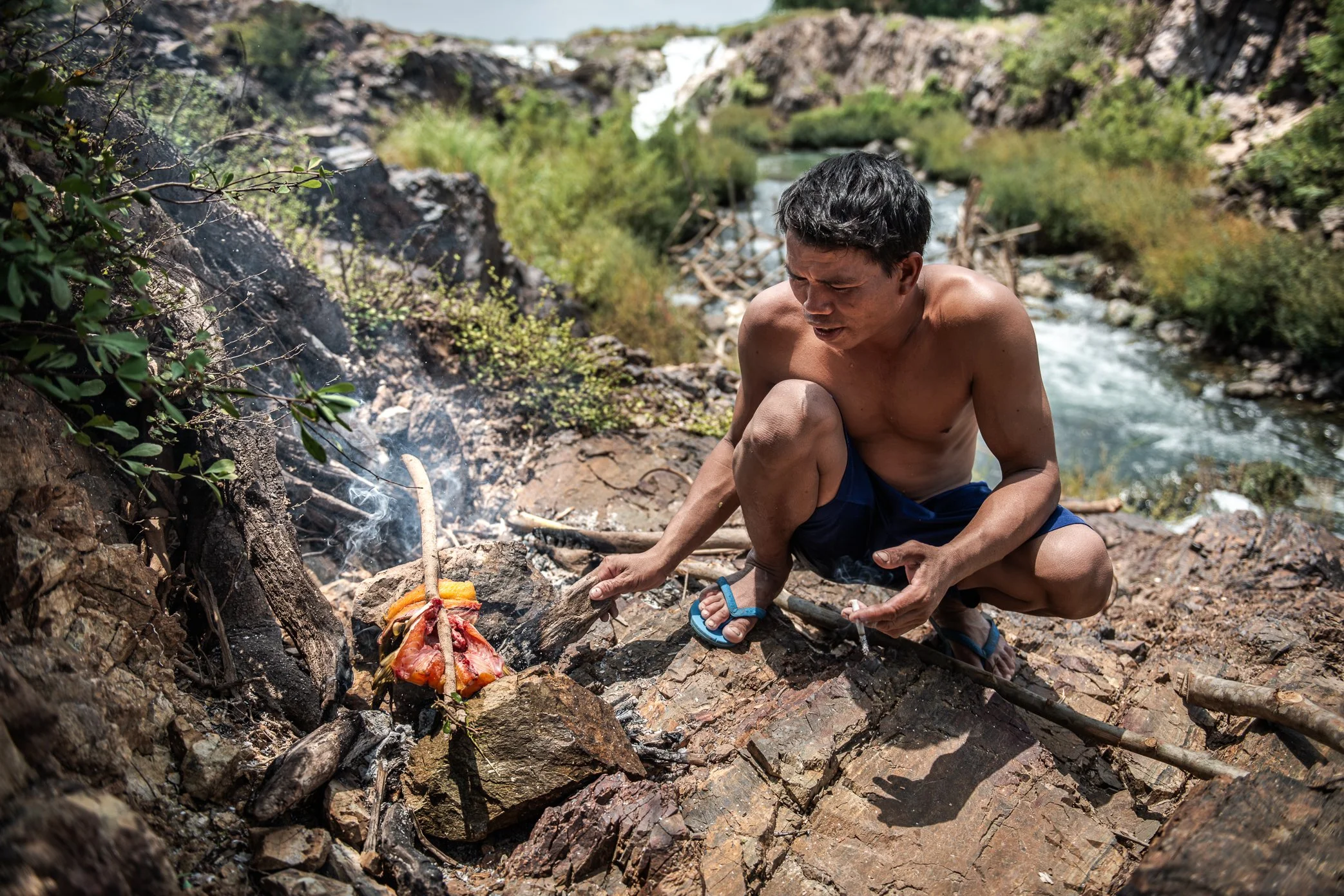 A fisherman prepares lunch beside a newly built Li trap in Si Phan Don. During long days on the rocks, men often rely on whatever the river provides near their work site - small fish caught from nearby channels, cooked over an open fire between round