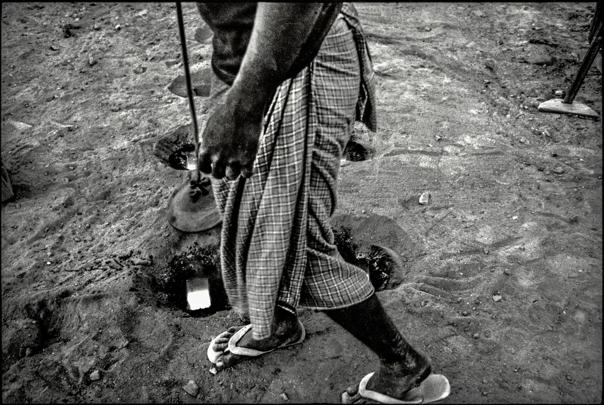 Patna, Bihar, India, April 2003 - A fire stoker prepares to feed coal into the kiln below. Beneath his feet, extreme heat rises through the firing chambers, separated from the workers above by little more than a layer of bricks and sand.