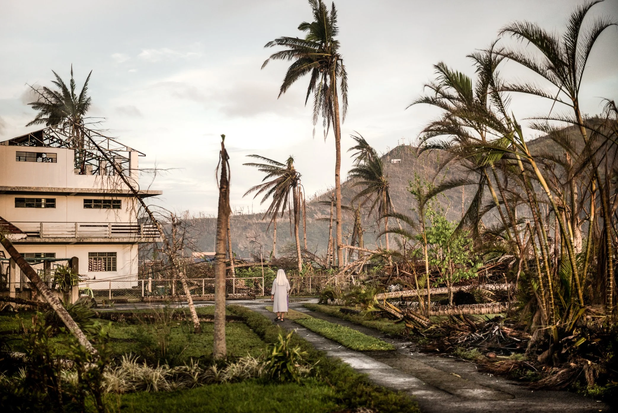 Palo, Leyte, Philippines, 2013 - A Catholic sister walks through the damaged grounds of a church complex after Typhoon Haiyan. Across Palo and nearby Tacloban, homes, churches, schools, and convents were damaged or destroyed, leaving religious commun