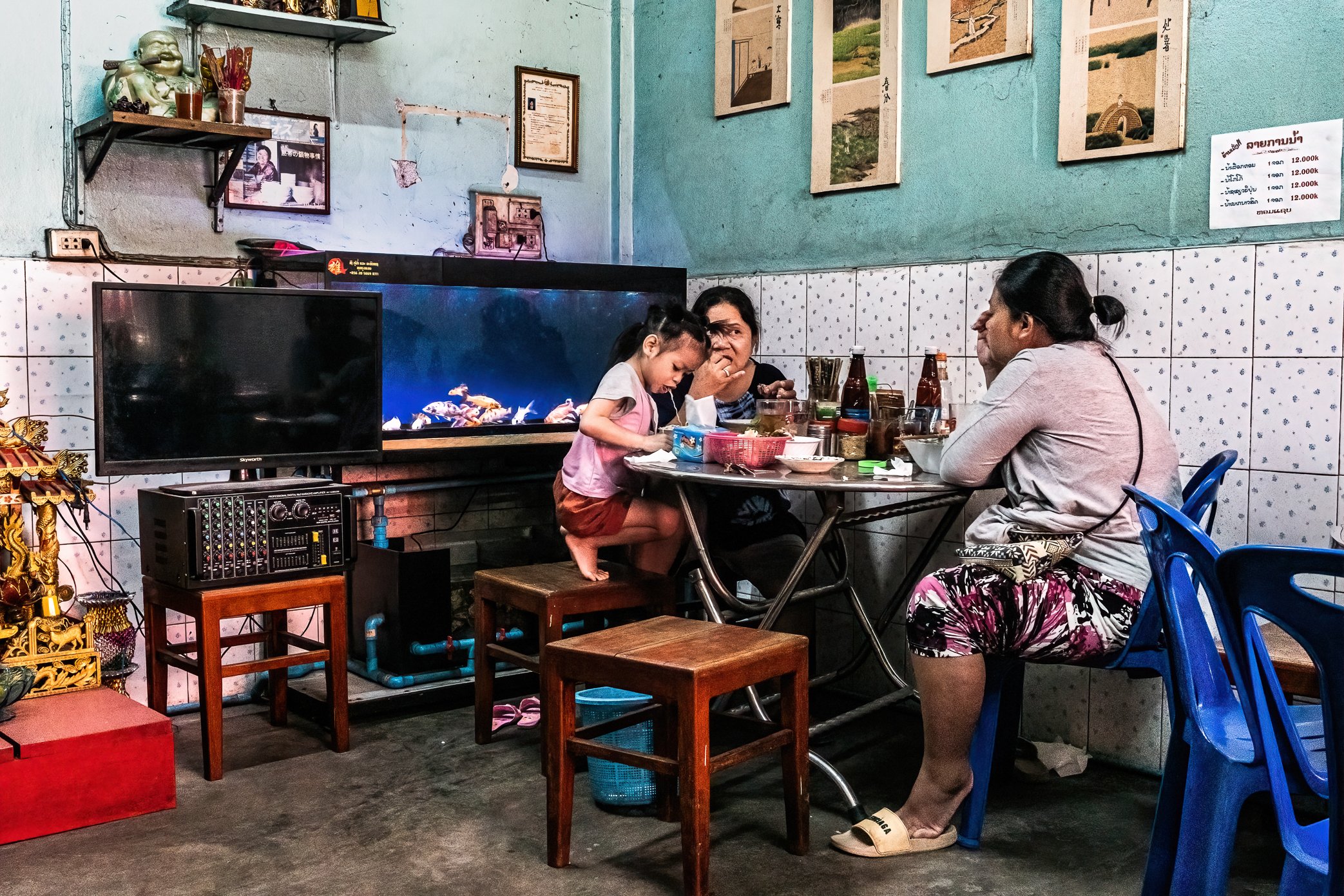 Pakse, Laos, 2022 - A family eats at a small street-food shop in Pakse. As inflation weakens household budgets, places like this remain an essential part of daily life - affordable, familiar, and close to home. For many Lao families, eating out no lo