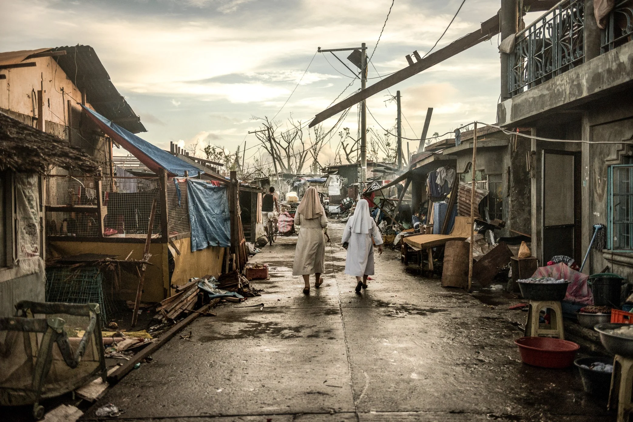 Palo, Leyte, Philippines, 2013 - Catholic sisters walk through a neighborhood devastated by Typhoon Haiyan, visiting families and offering support in the days after the storm. Around them, homes remain damaged and streets are lined with debris, but t