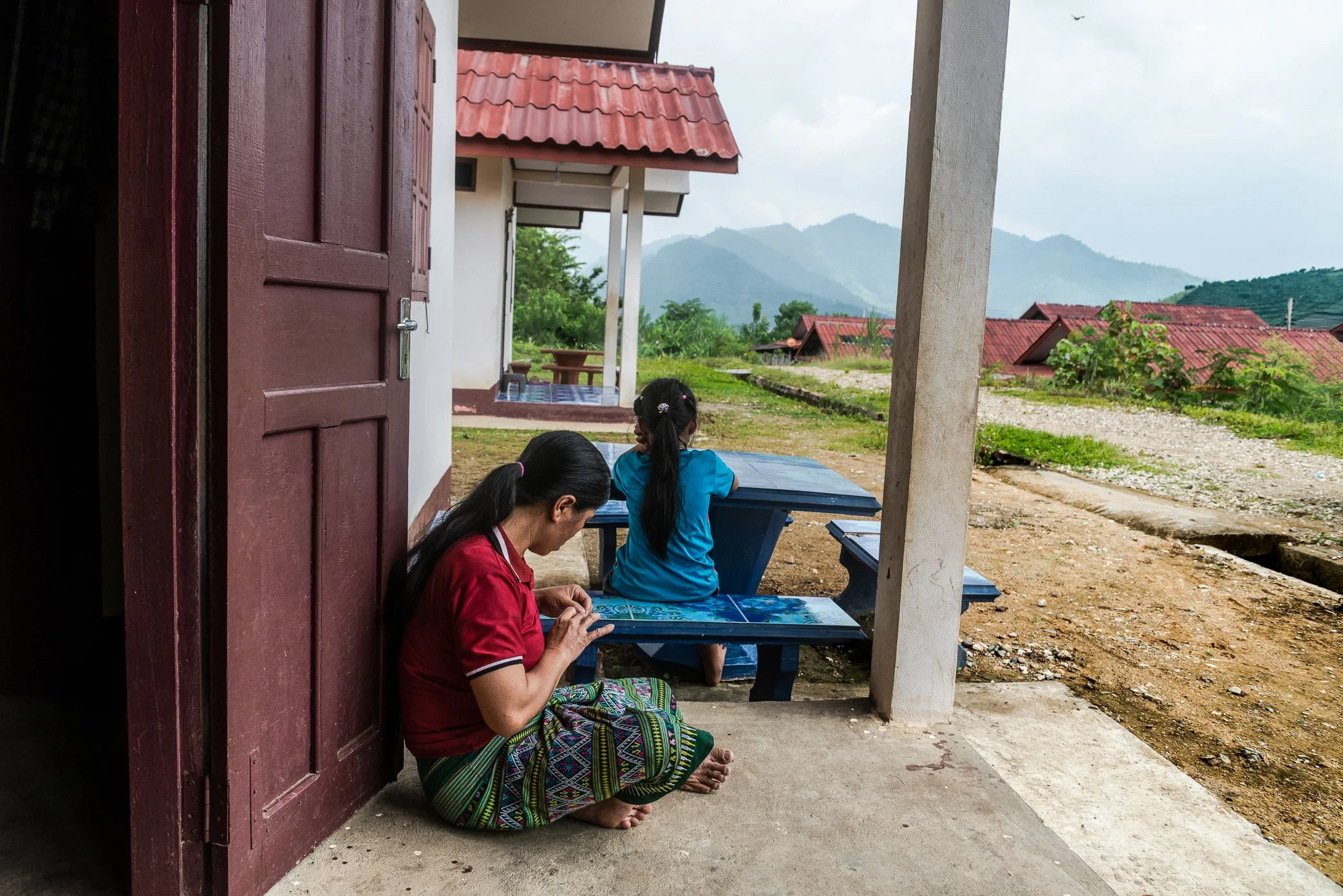 A woman and a child sit outside a resettlement house near the Luang Prabang hydropower project, in an area where families were moved from villages affected by dam construction.

For many rural communities in Laos, a house is not only a place to live.