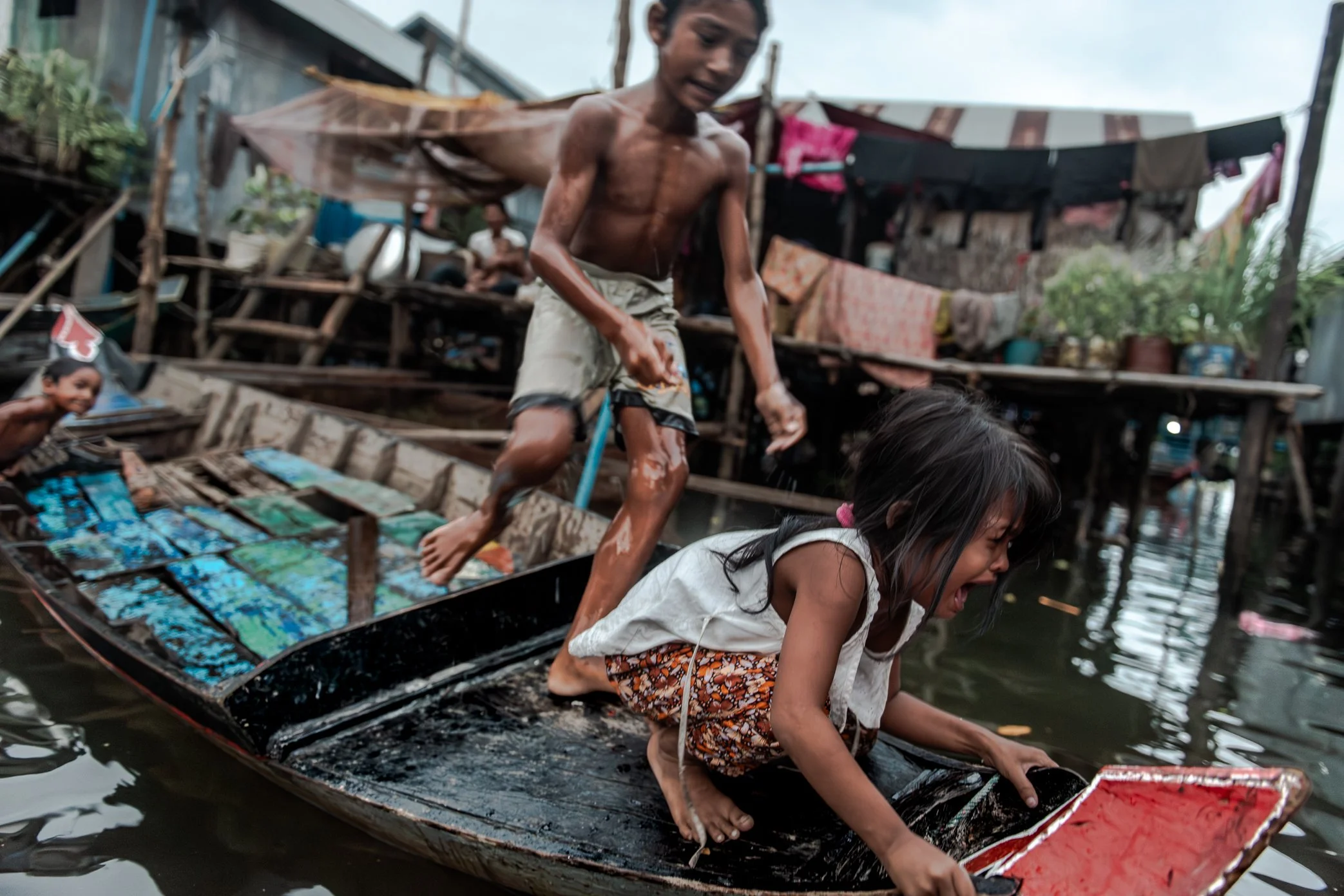 Children move between boats in Kampong Phluk, where daily life is lived on and above the water. In the floating village, even a short journey from one home to another can mean stepping across narrow boats, wet wooden edges, and shifting platforms. Fo