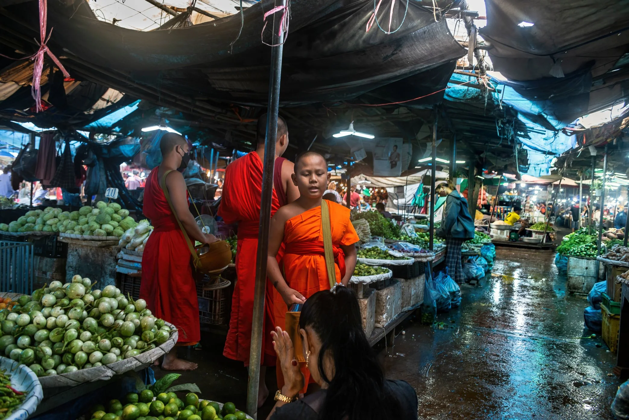Vientiane, Laos, 2022 - Monks receive morning offerings from vendors at Oxy wholesale fresh market, where faith and commerce meet before the day’s trading begins. As Laos faces rising prices, a weakened kip, and the wider effects of global economic s