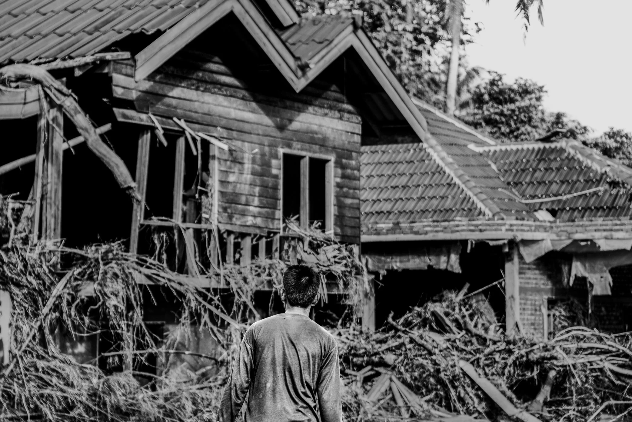 Hin Lat Village, Attapeu, Laos - A survivor stands before damaged homes in Hin Lat after the Xe Pian dam collapse. Scenes like this were visible throughout the village: houses torn open, walls broken, and debris left hanging from the structures that 