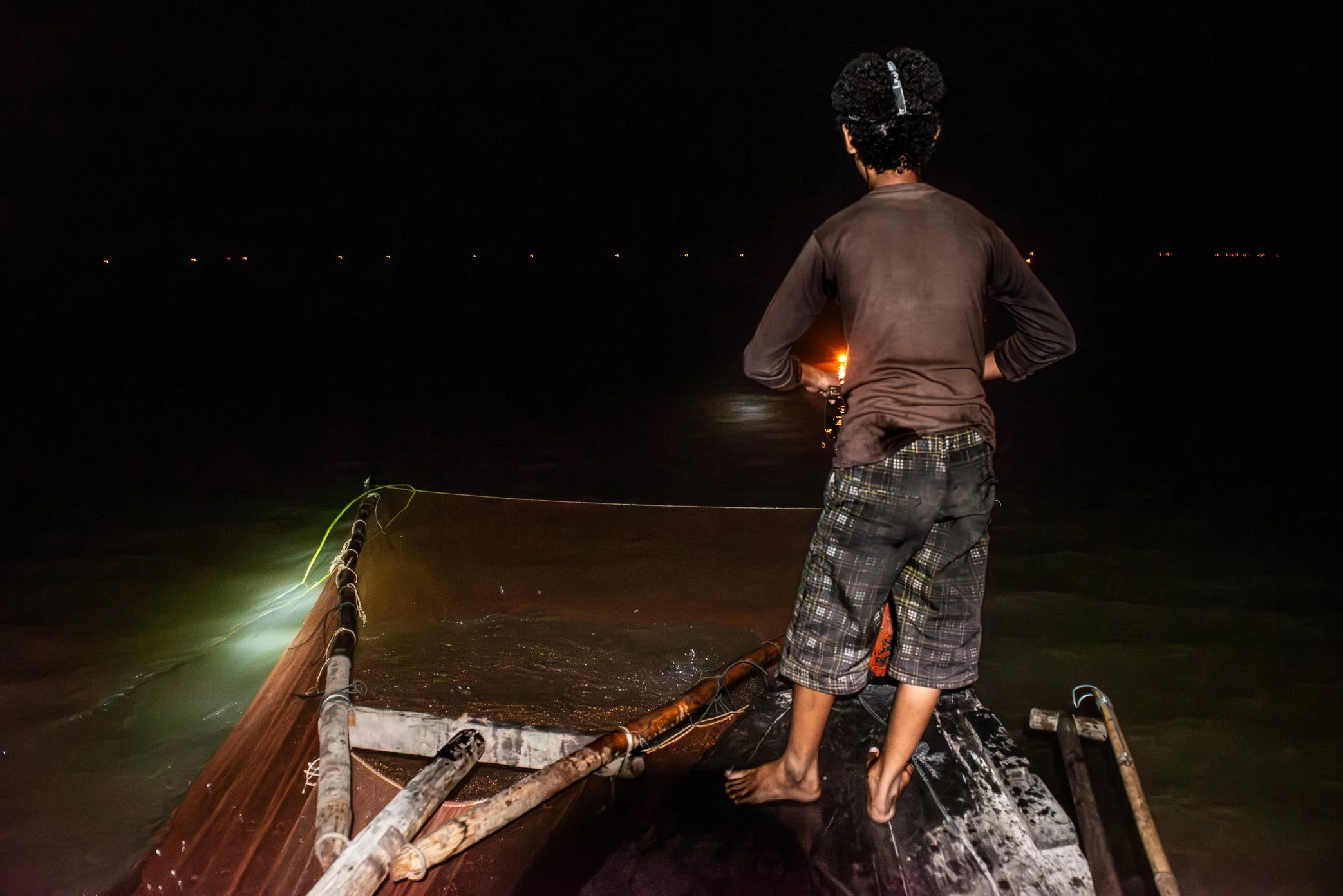 Tonle Sap, Cambodia - When the time comes, fishermen move from lamp to lamp across the dark water. A large scoop net, built onto the front of the boat and adapted for this method, is lowered beneath each kerosene flame. One person stands at the bow t