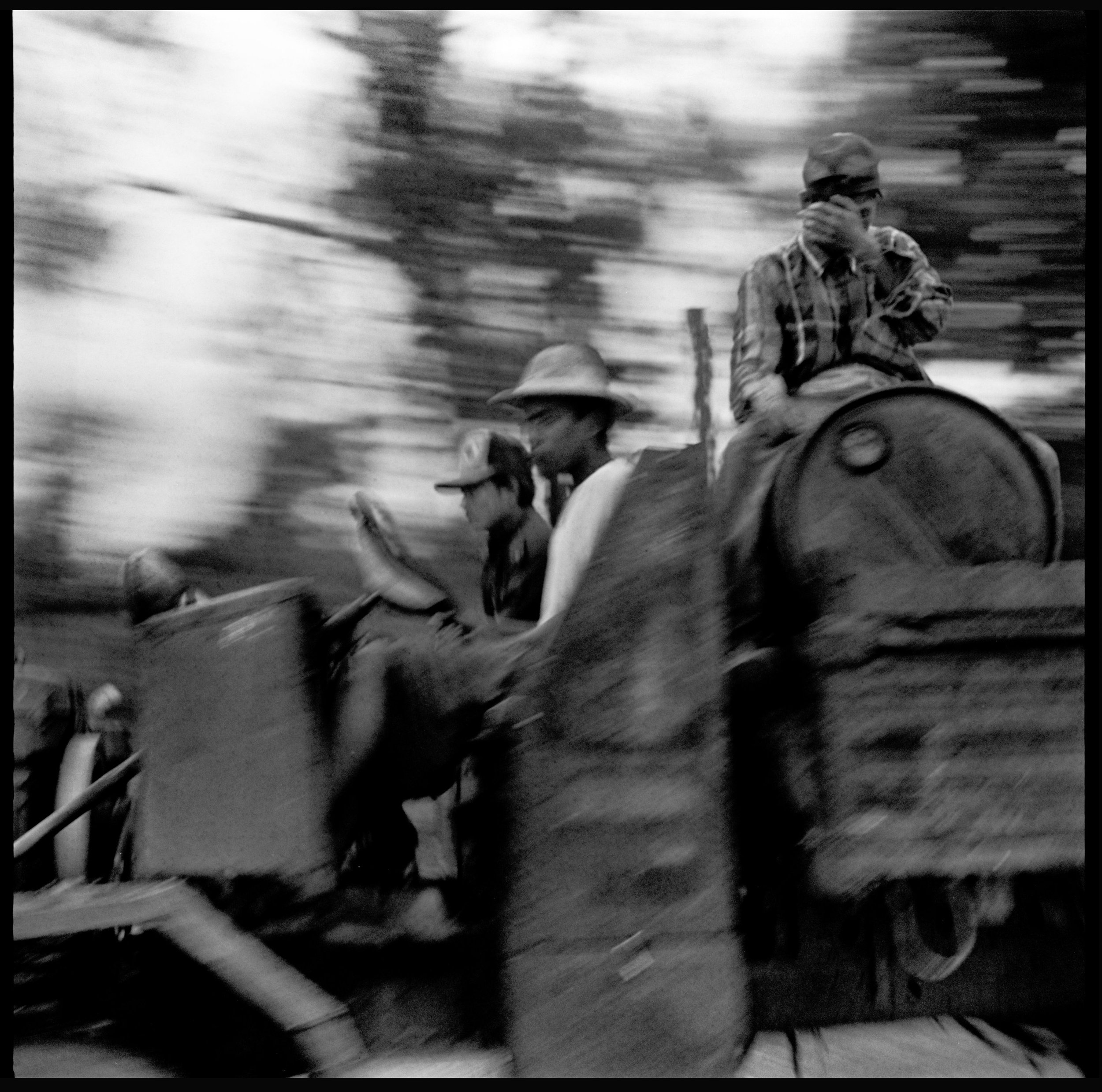 Black and white photo of three children riding on a moving train or tram, with a blurred background indicating motion.