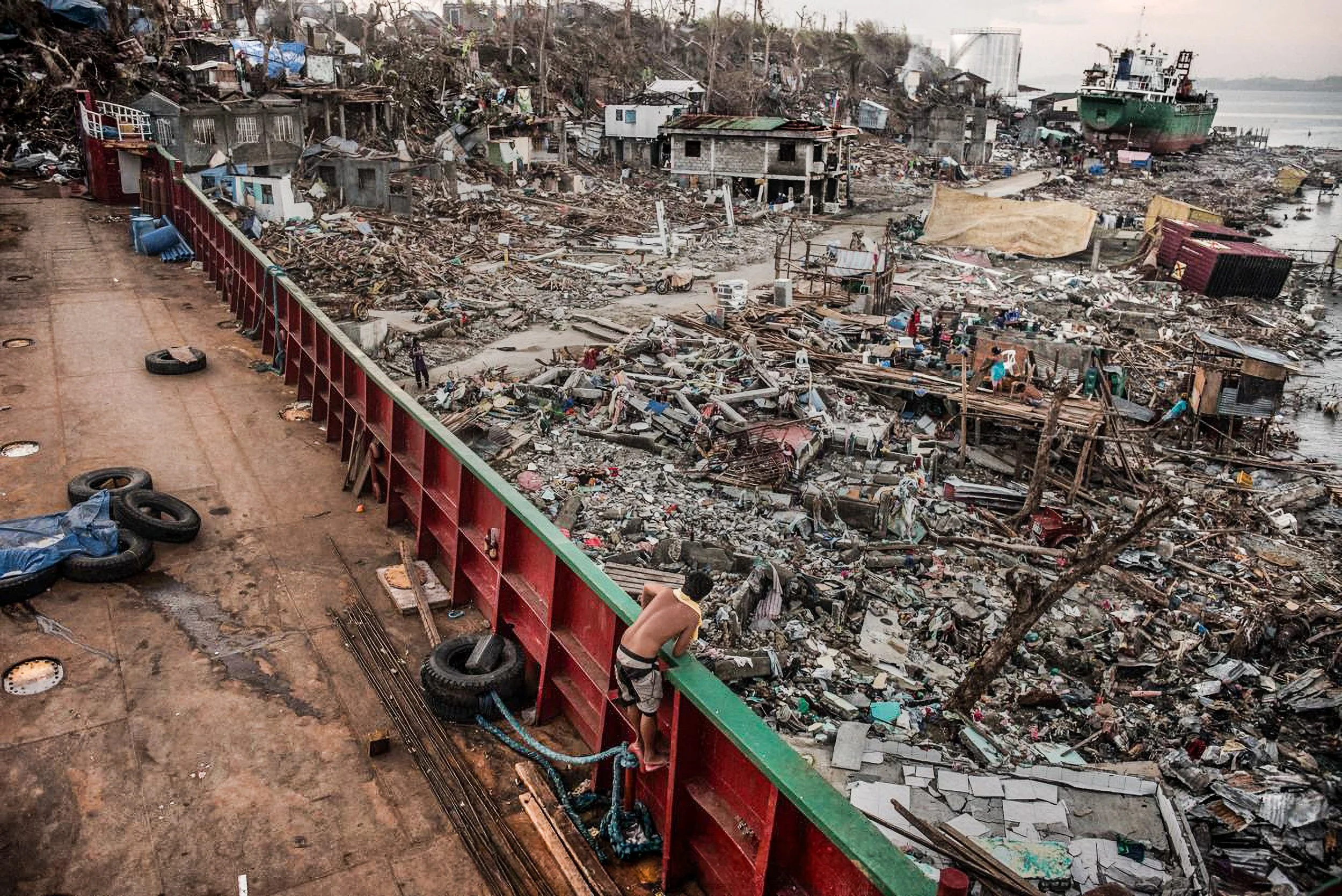 Tacloban, Philippines, 2013 - From the deck of a wrecked ship where survivors had taken shelter, the scale of Typhoon Haiyan’s destruction stretches toward the sea: flattened homes, scattered debris, and other vessels driven ashore by the storm.
