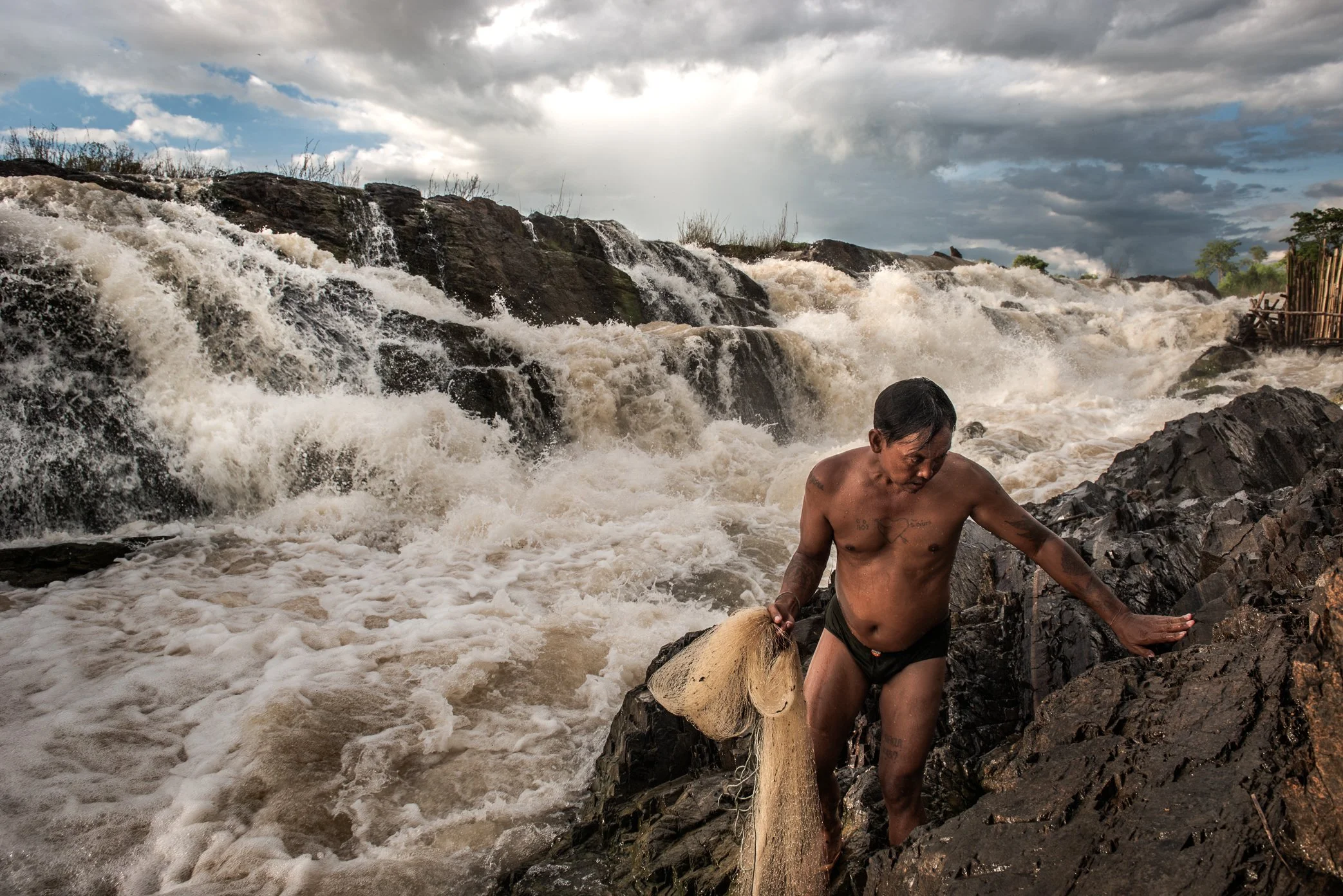 Before returning home after a day on the rocks, a fisherman casts a small net in the torrent below the falls, gathering fish for the evening meal. In Si Phan Don, where the Mekong breaks into channels, rapids, and waterfalls, fishing is not only a ma