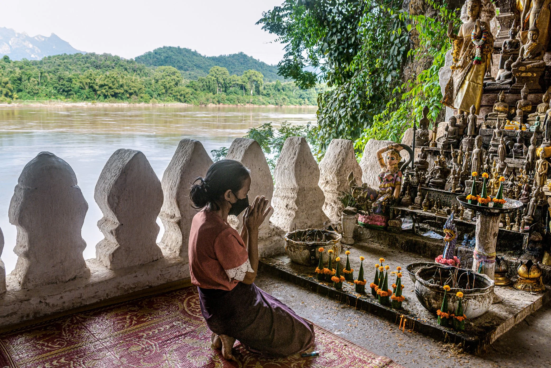 A souvenir seller prays inside Tham Ting, part of the Pak Ou Caves, a sacred cliffside site overlooking the Mekong opposite the mouth of the Nam Ou. Reached only by boat, the caves have drawn pilgrims, villagers, and tourists to Luang Prabang for gen