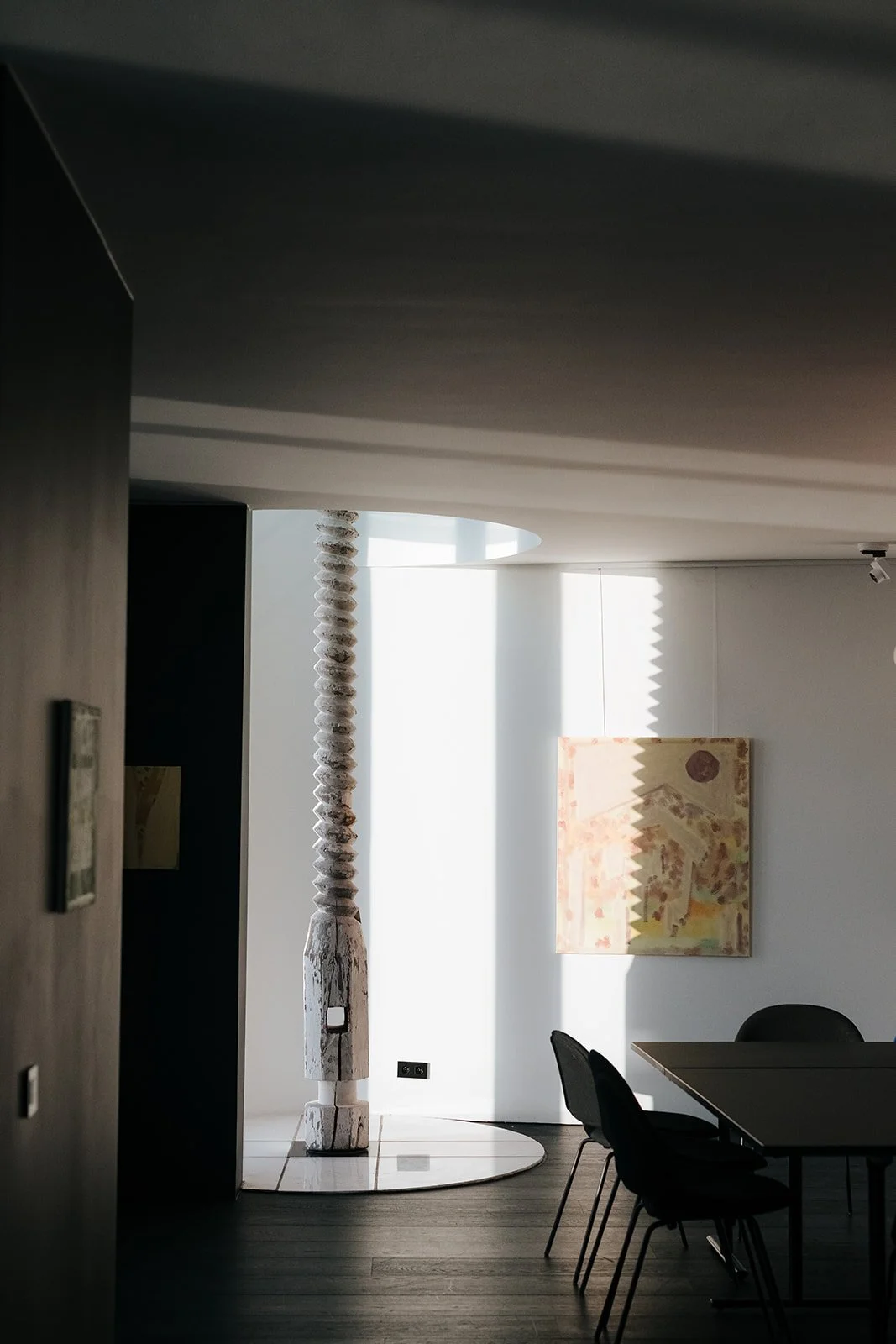 Interieur van het Huis van Roosmalen modern kantoor of galerij met wit en zwart decor, een houten sculptuur en een abstract kunstwerk aan de muur, verlicht door natuurlijke lichtinval.