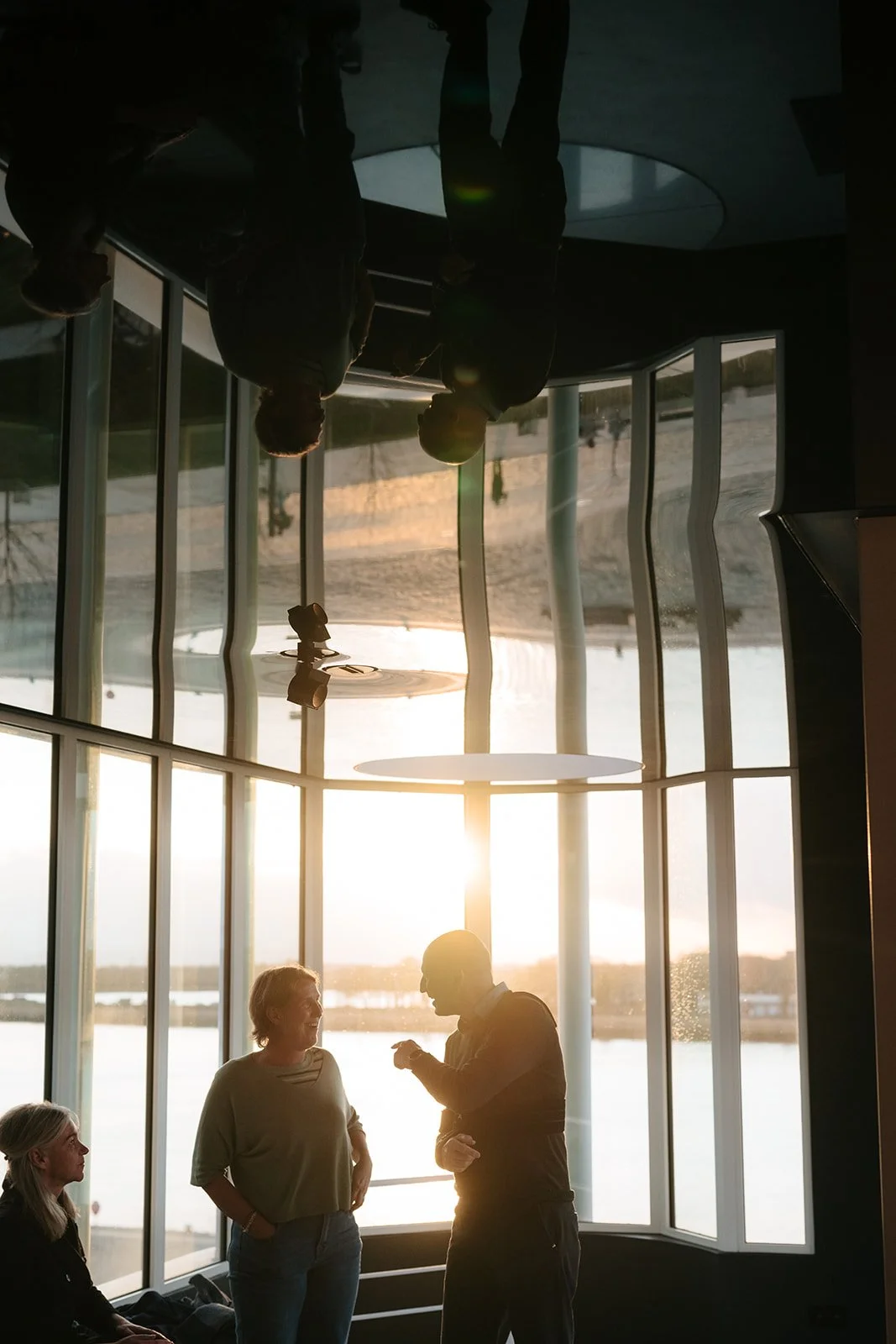 Mensen bij een raam met uitzicht op de Antwerpse Schelde tijdens zonsondergang, binnen het Huis van Roosmalen.