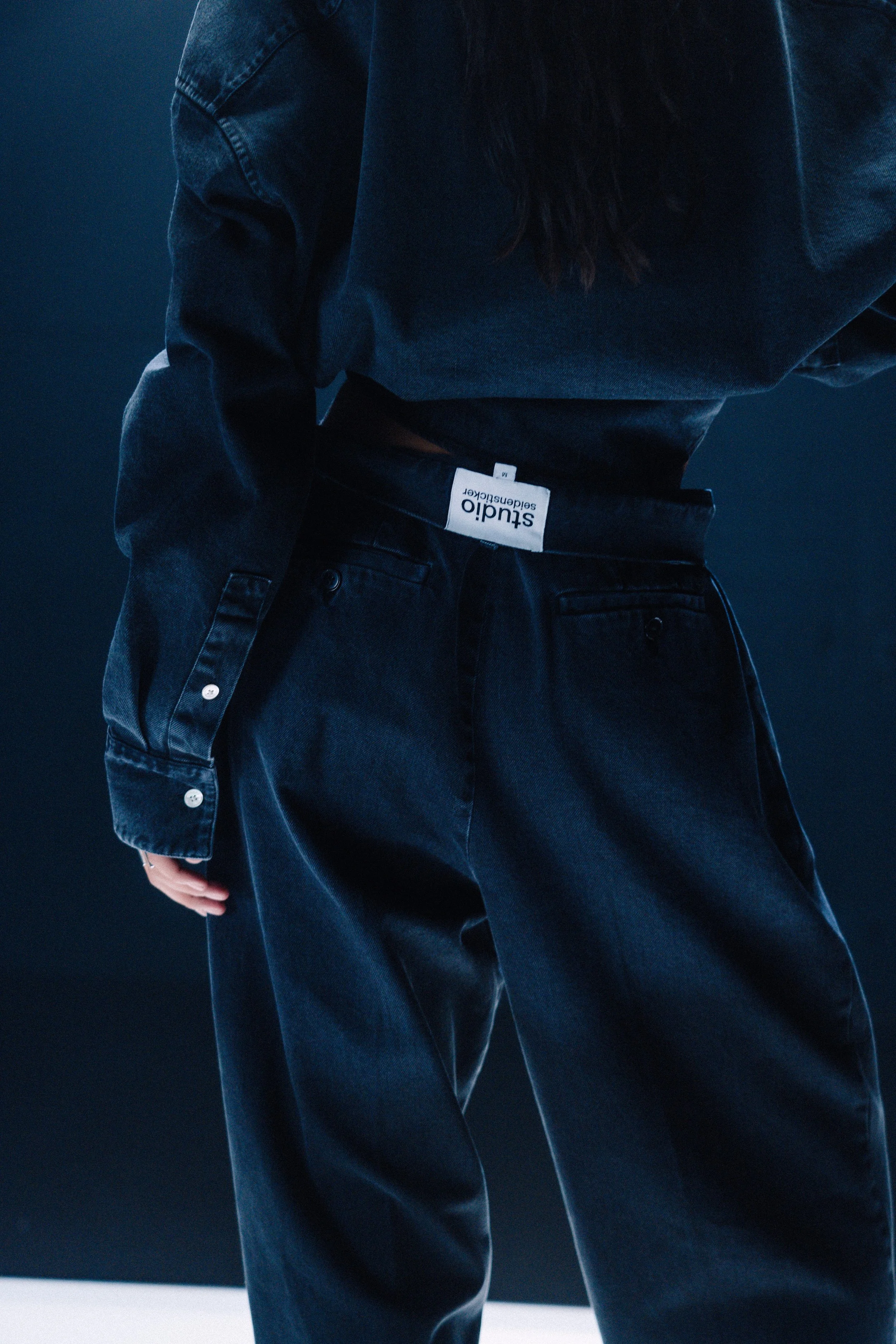 Nahaufnahme einer Person in dunkler Jeans und Jacke auf einem dunklen Hintergrund.