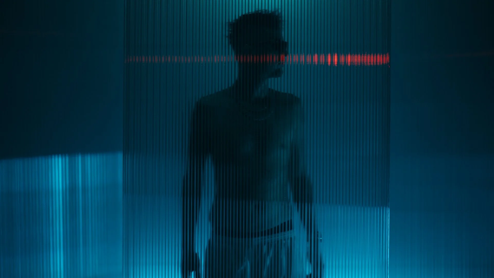 Robin Schulz steht hinter einer transparenten, ribbeligen Scheibe, beleuchtet mit bläulichem und rotem Licht.