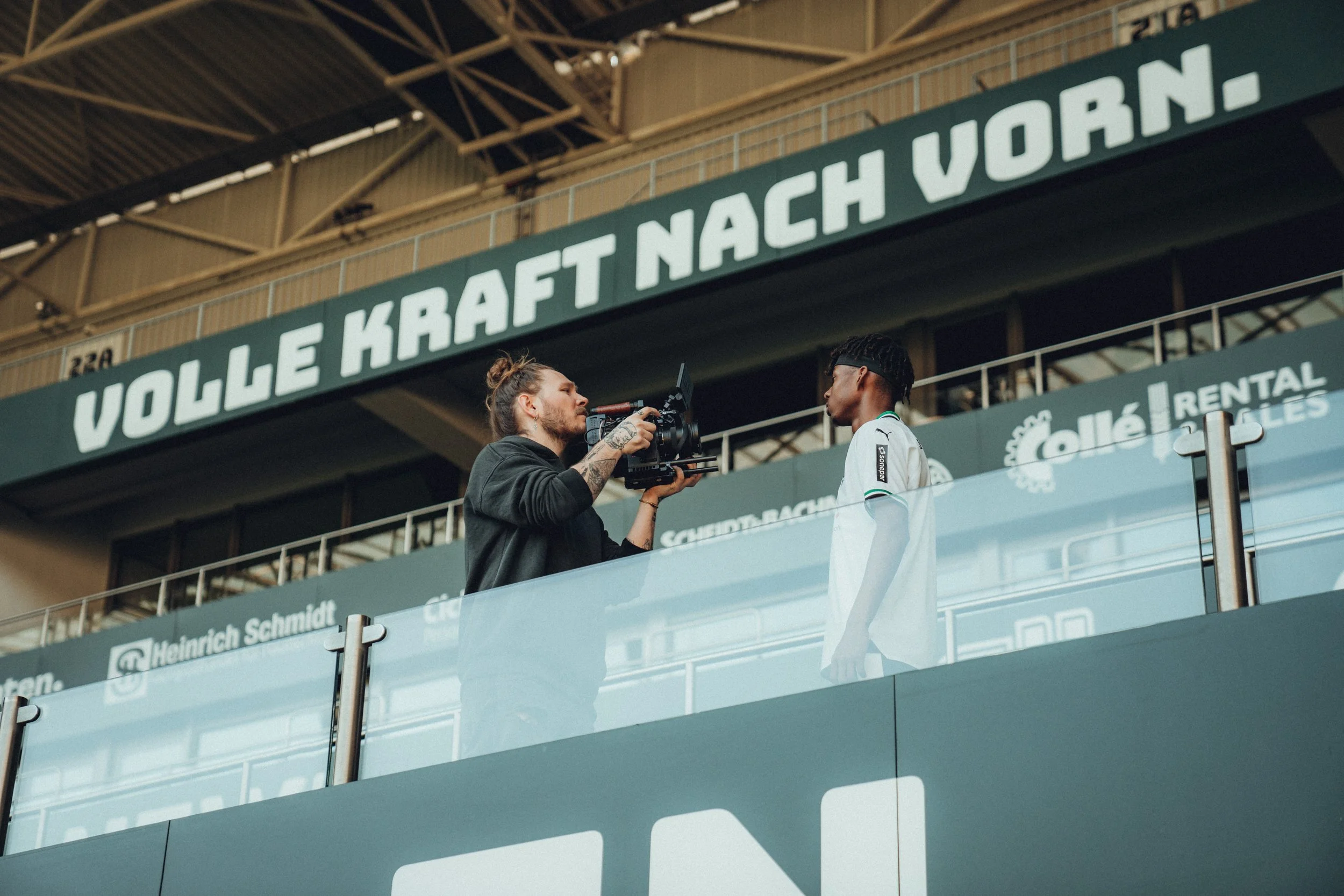 Levi Stute filmt einen Fußballspieler mit einer Kamera auf einer Tribüne in einem Stadion.